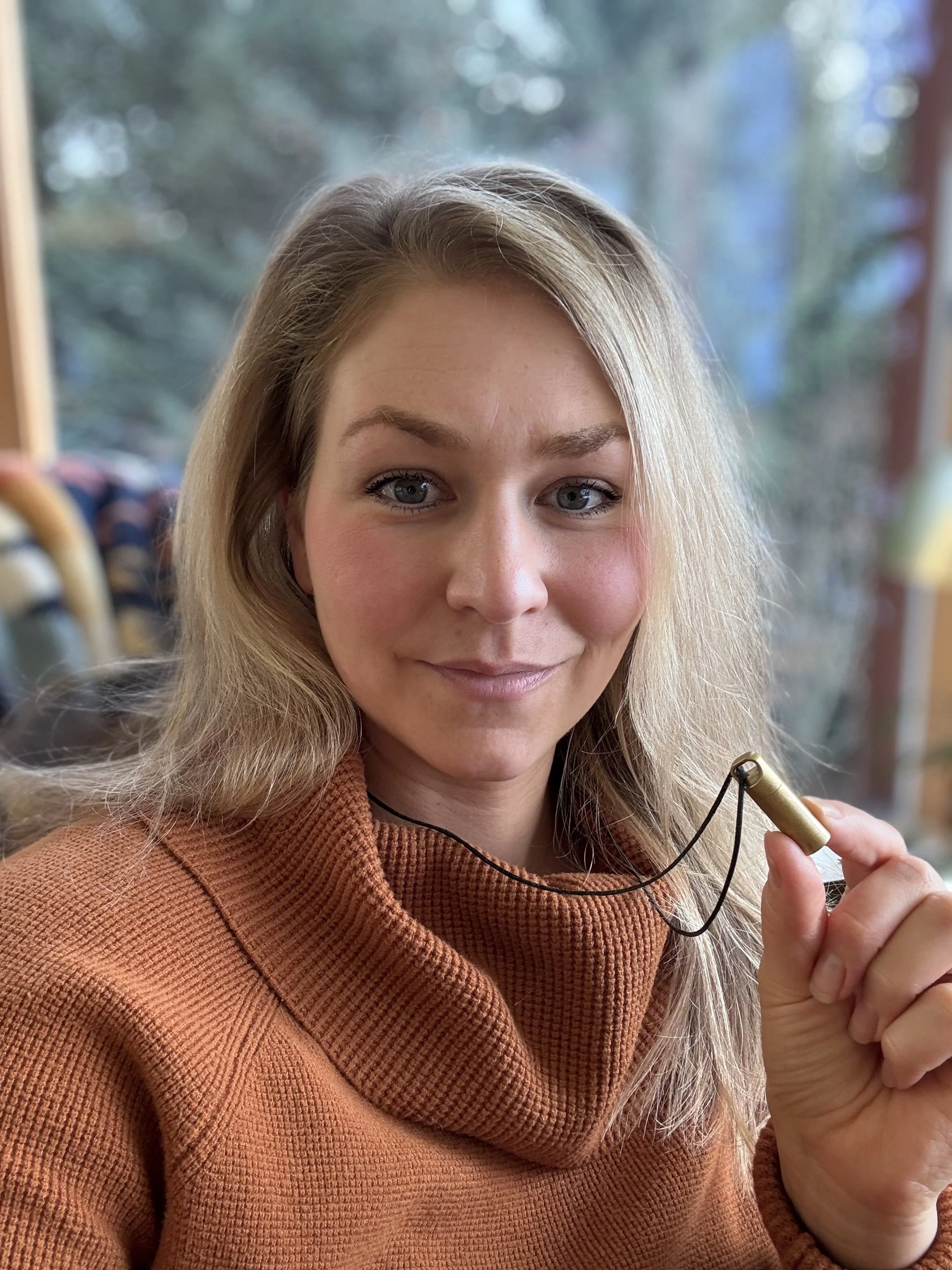 woman holding up a necklace with a gold capsule