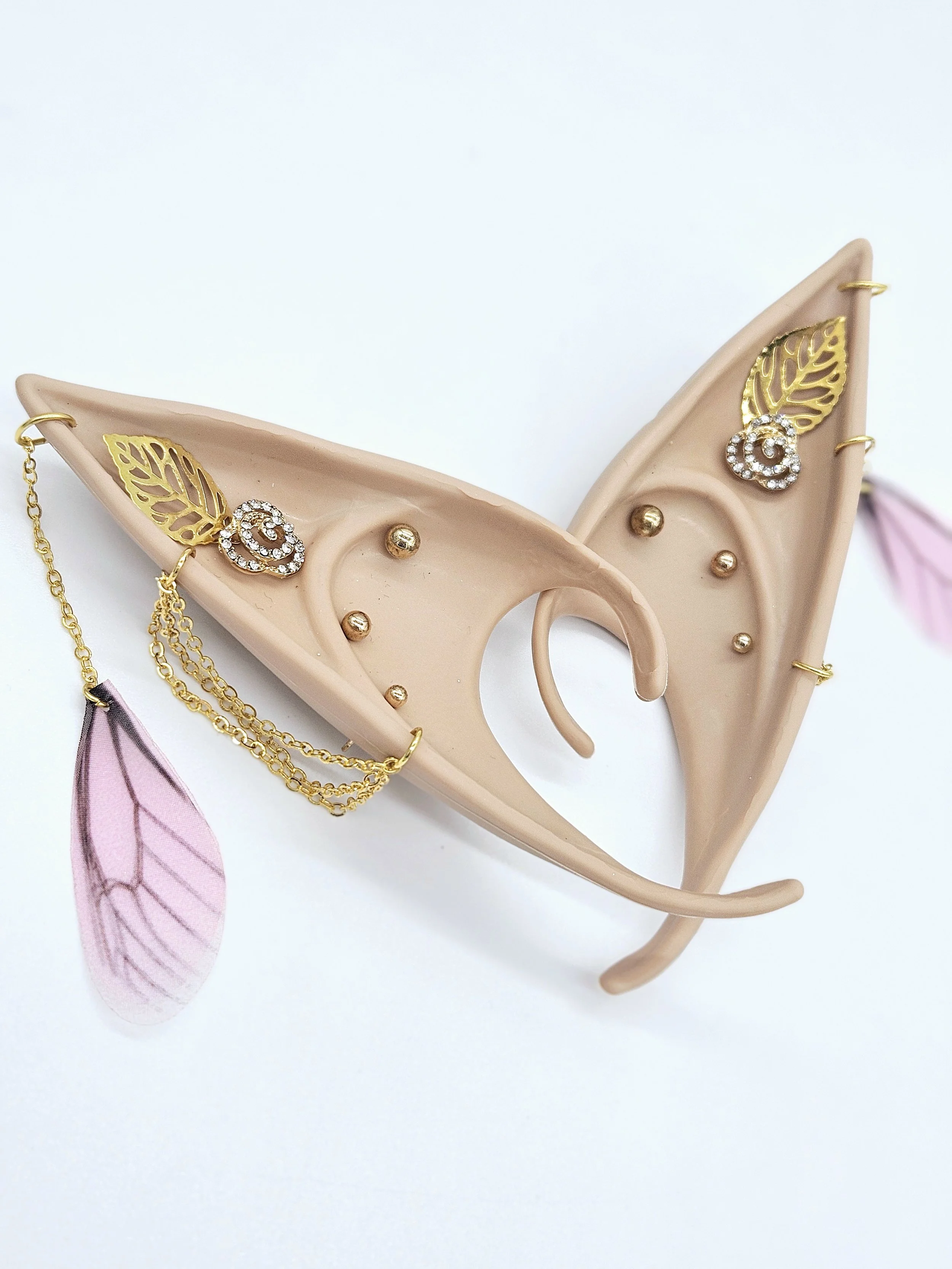Pink high heel shoe with gold jewelry, including a leaf-shaped earring with a diamond spiral and gold chains, on a white background.