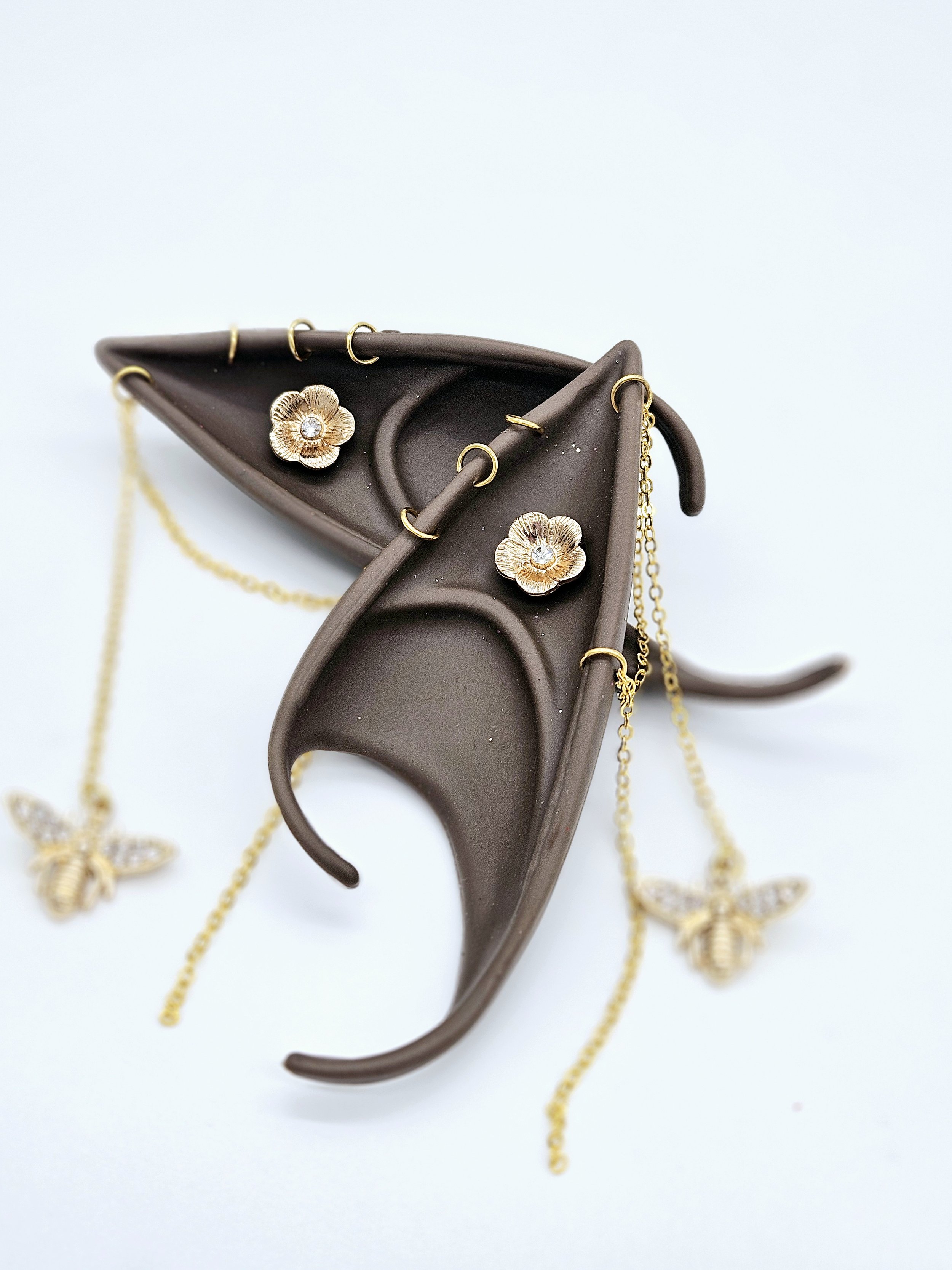Gold jewelry with floral and butterfly designs arranged on a dark brown jewelry tray.