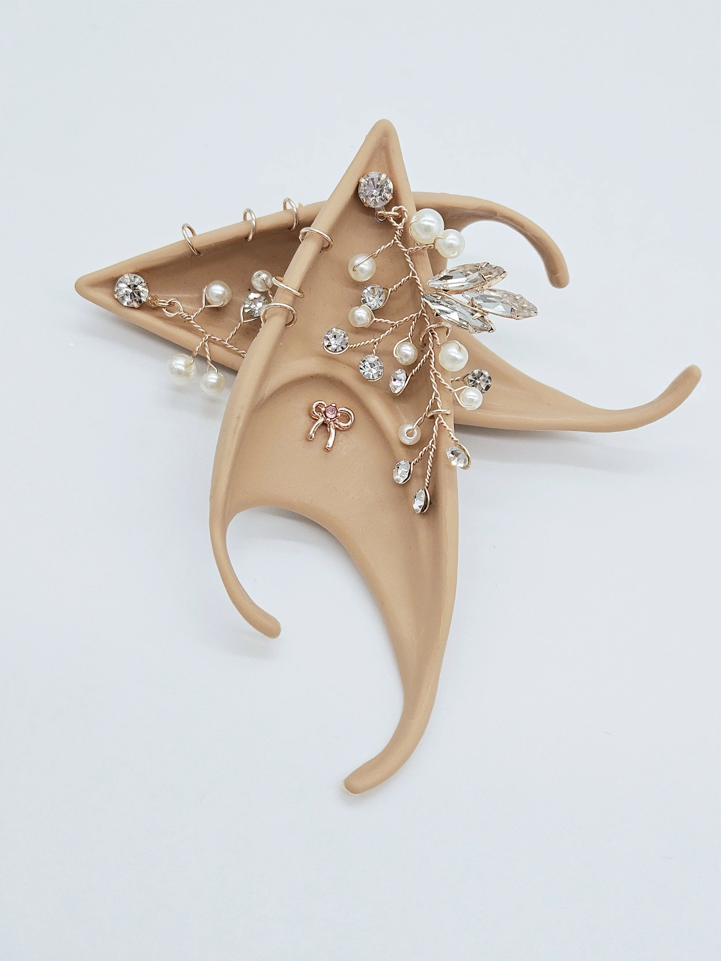 A beige ear-shaped jewelry holder with multiple earrings, including pearl and crystal designs, displayed on a light background.