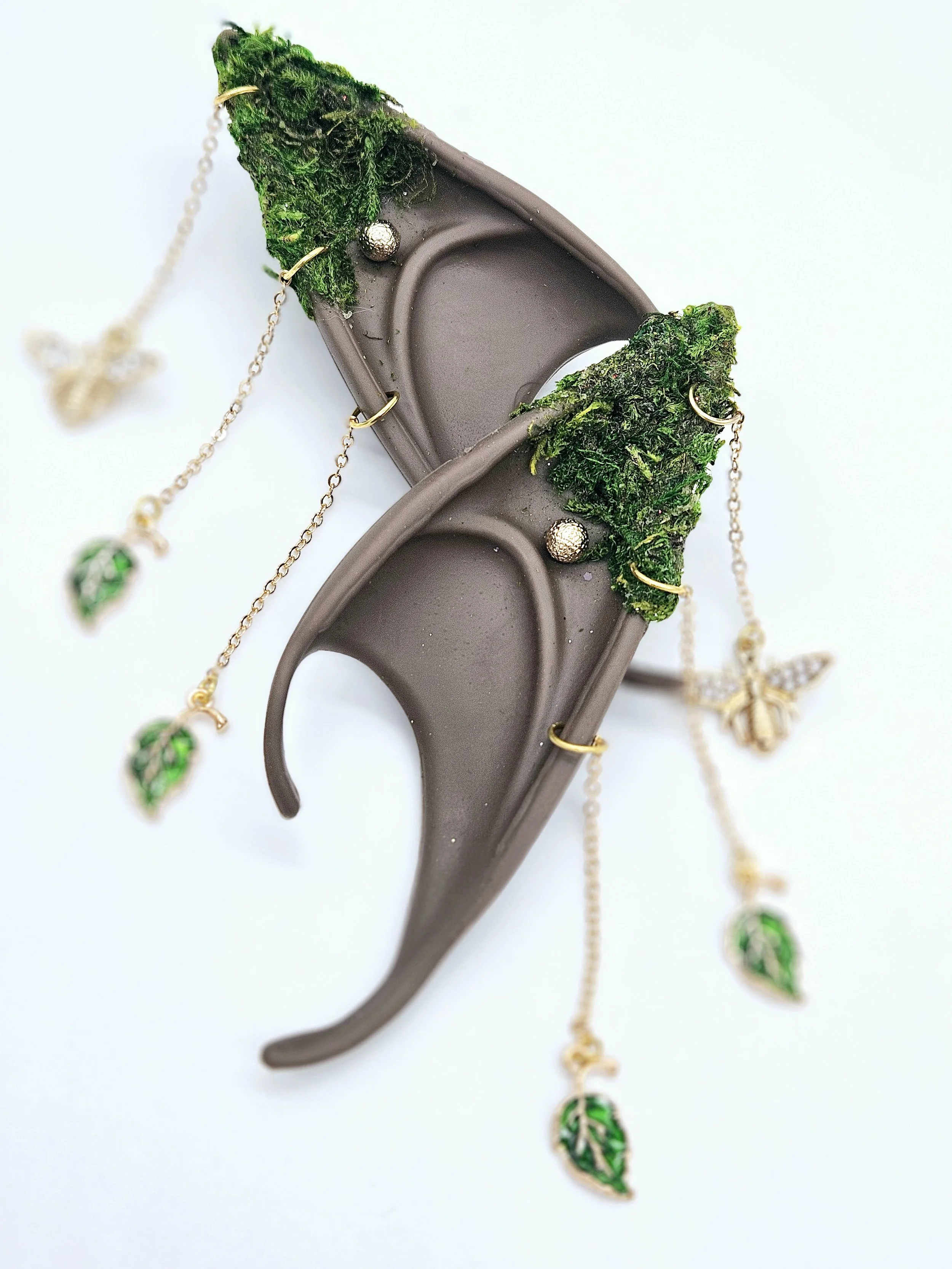 A brown plastic hair clip decorated with green moss and small gold balls, with gold chains hanging from it that have green leaf charms.