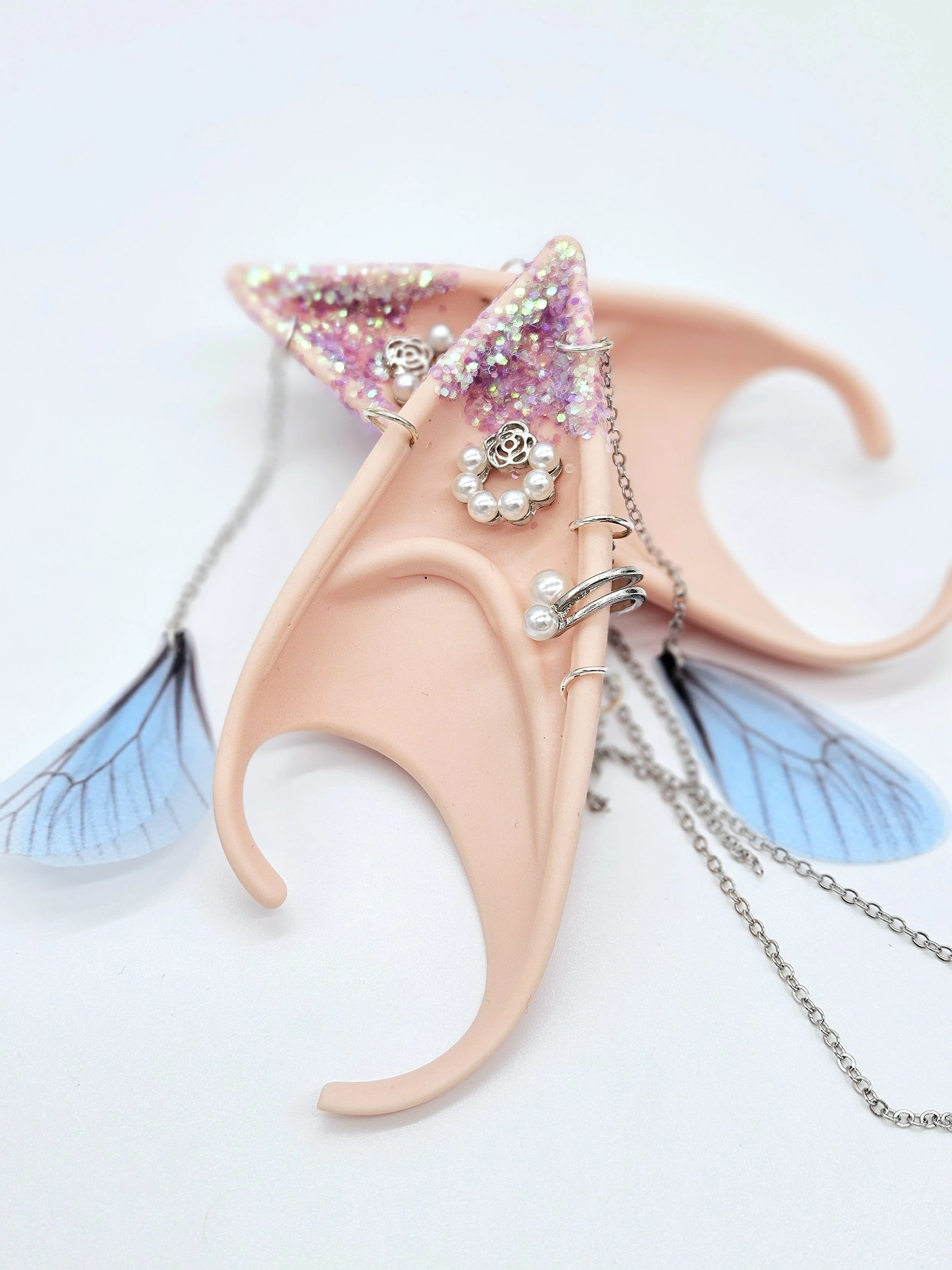 Close-up of a pink decorative jewelry display with glitter, featuring earrings, rings, and chains, all arranged on a pink plastic star-shaped holder with light blue butterfly wings attached.