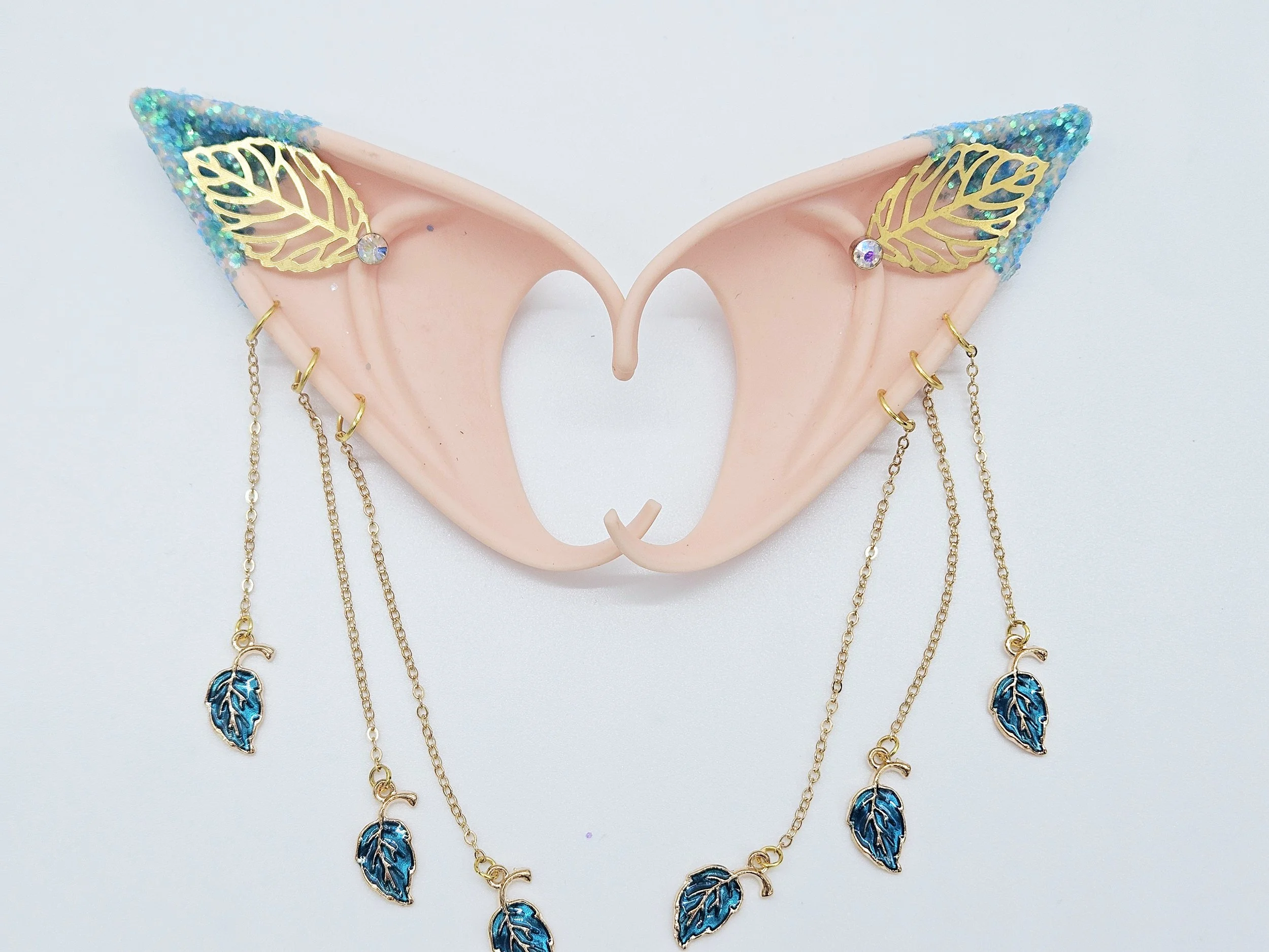 A collection of gold jewelry with blue and black leaf designs hanging from a pink decorative holder with glitter accents.