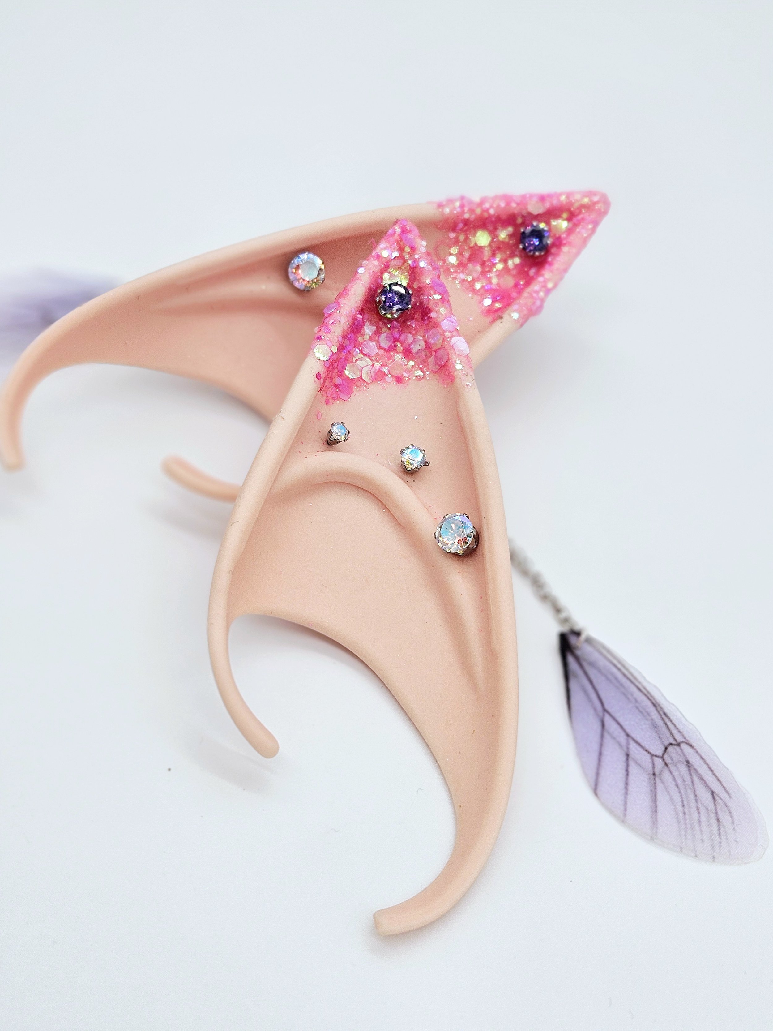 A pink plastic earring with rhinestones and a purple leaf attached to a transparent wire.