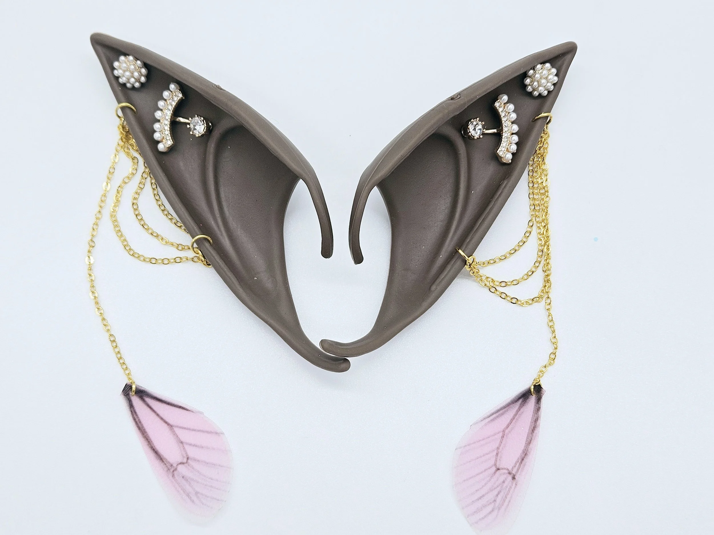A decorative display of a pair of felt high-heeled shoes adorned with pearl and crystal jewelry, with pink translucent leaves hanging from the heels, against a plain white background.