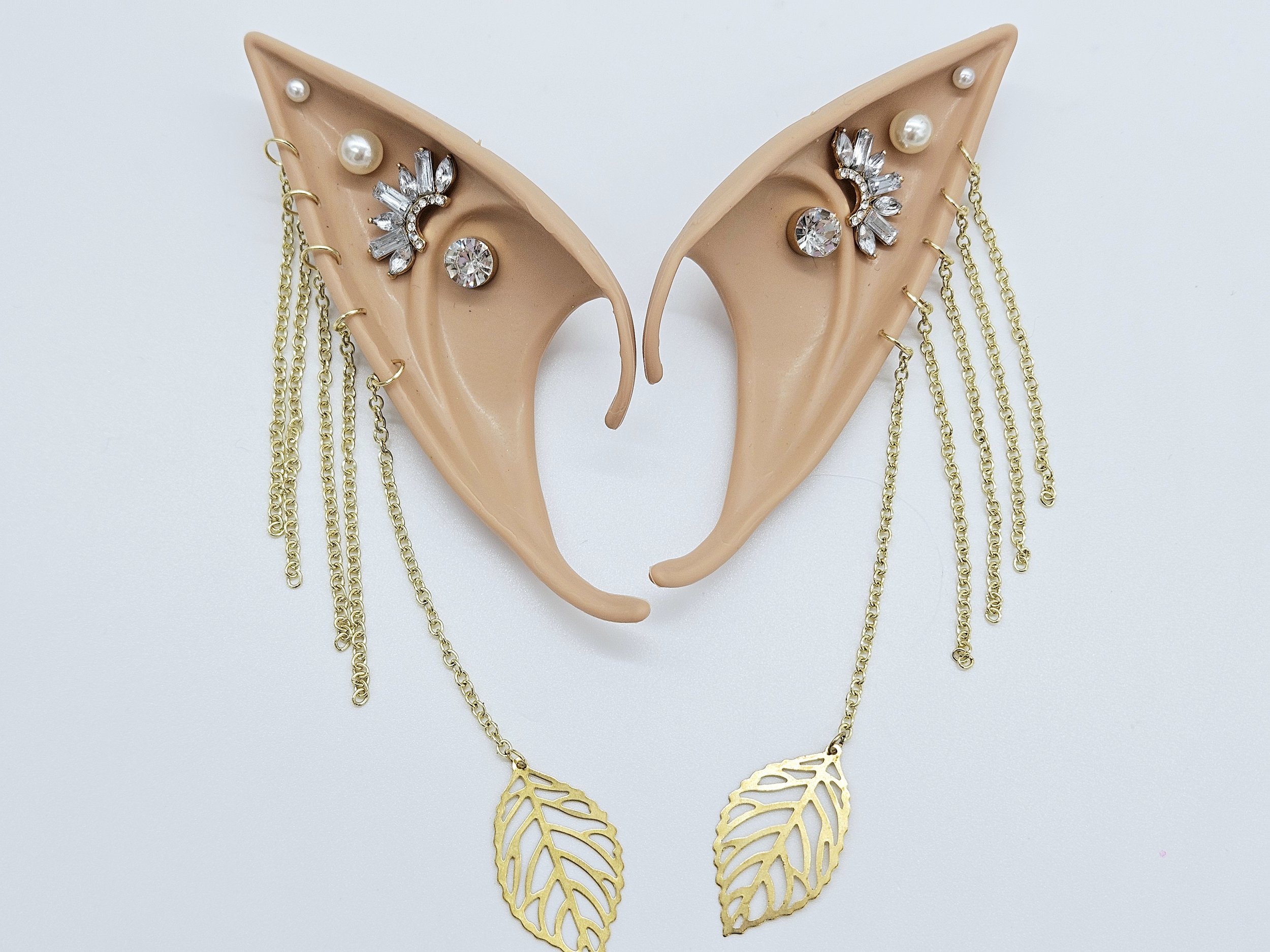 A display of jewelry that includes earrings, necklaces, and chains shaped like leaves, with some earrings decorated with pearls and rhinestones, arranged on beige ear-shaped stands.