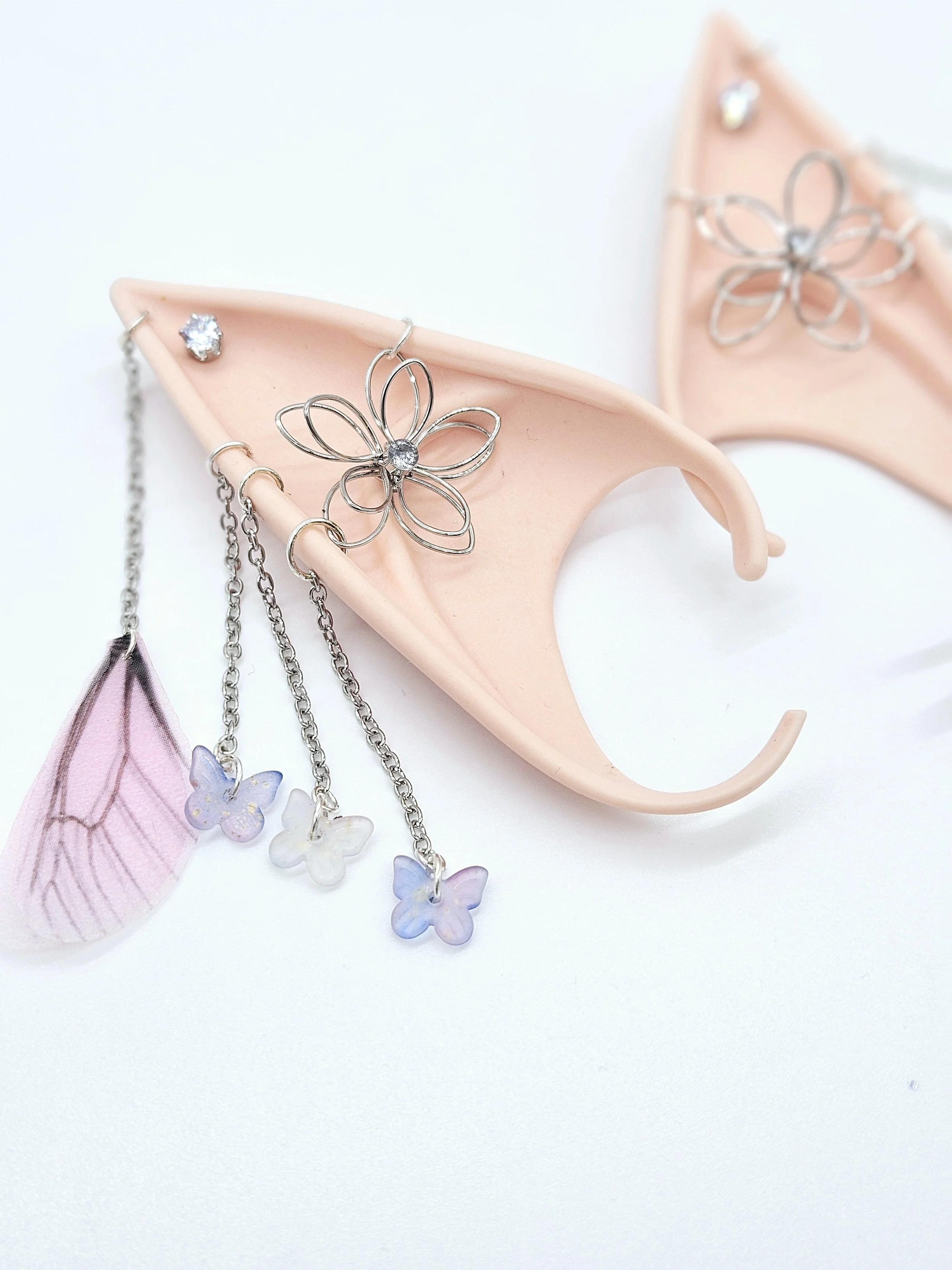 Pink ceramic dish holding jewelry, including silver flower-shaped necklace with a rhinestone center, small rhinestone stud, and dangling earrings with pastel flower-shaped charms.