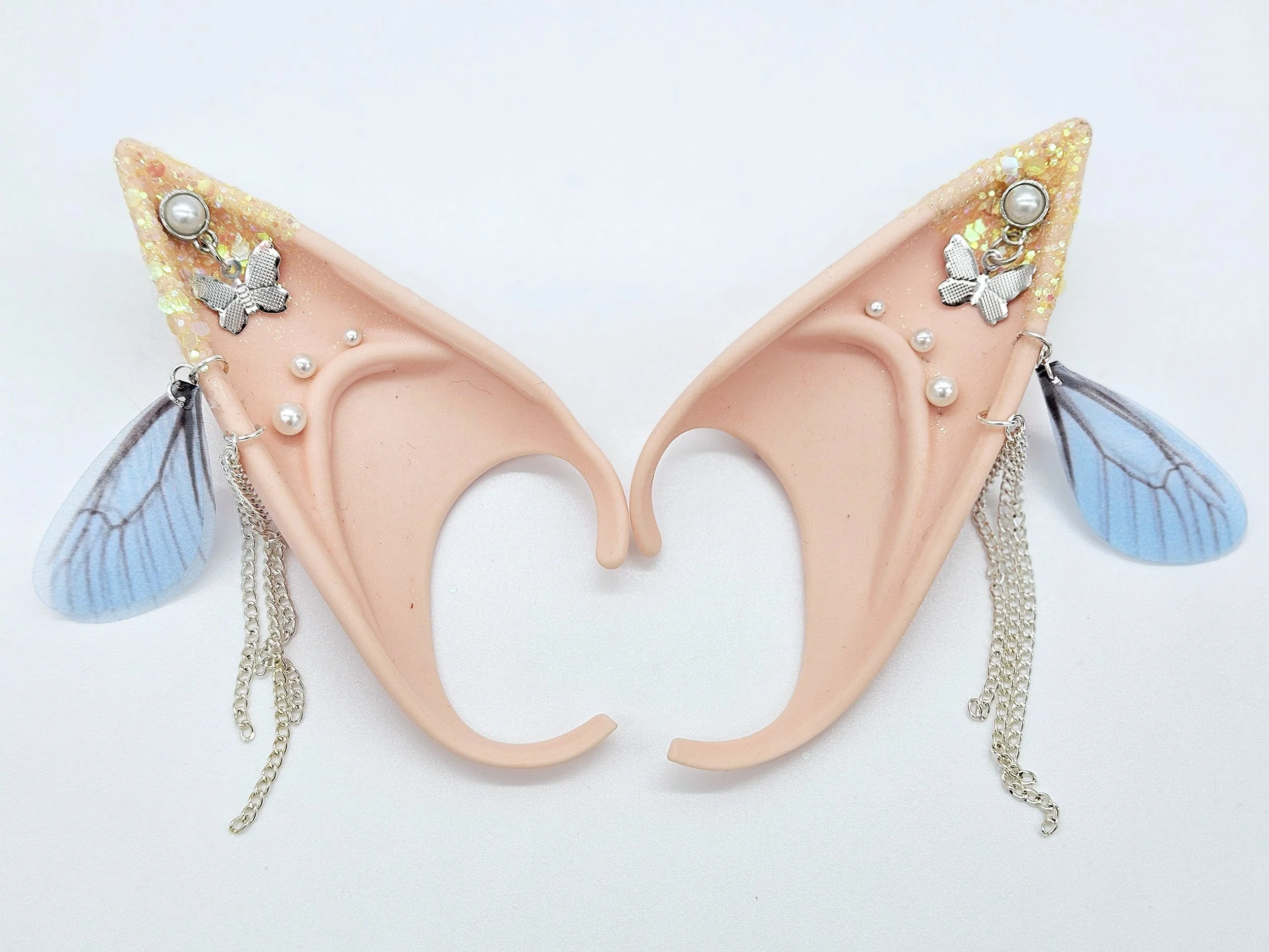 A pair of decorative fairy ear accessories with butterfly and pearl embellishments, featuring translucent blue wings and hanging silver chains.