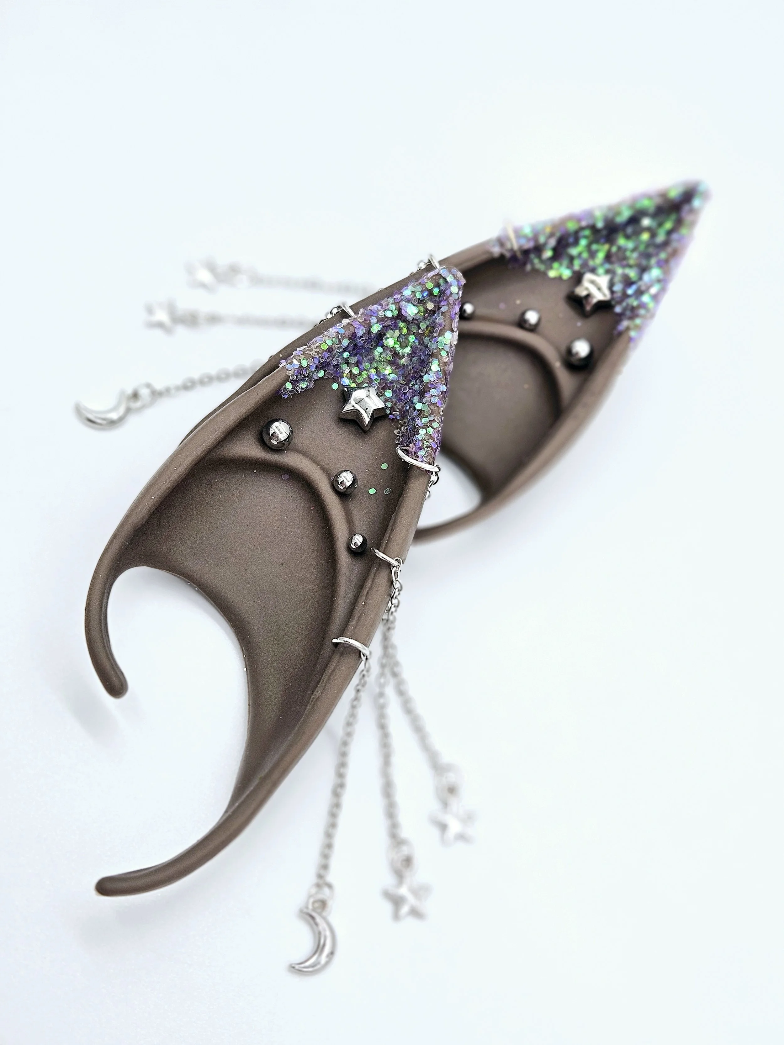Close-up of silver jewelry shaped like moons, stars, and glittery areas on a plastic animal or object, with a chain and stars hanging from it.