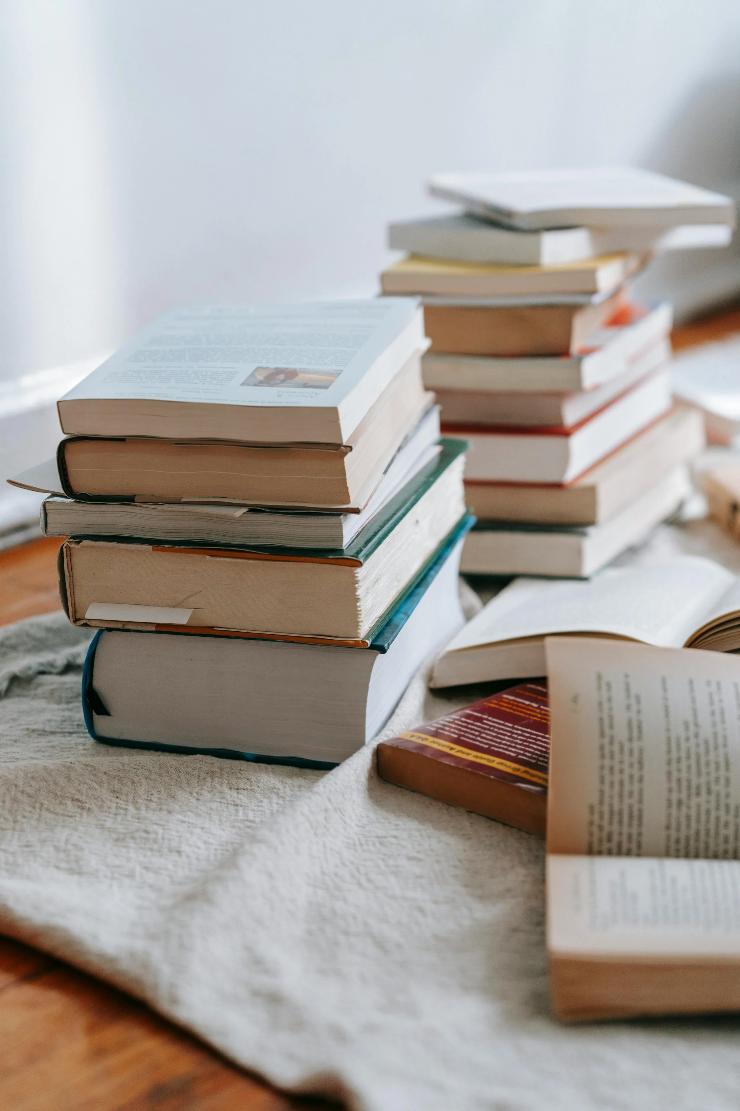 Stacks of open and closed books placed on a beige cloth on a wooden surface, with some books open showing pages.