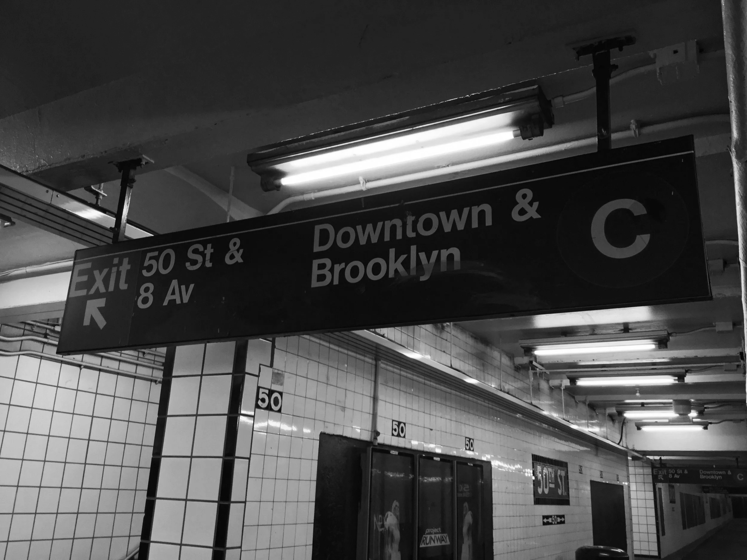 Black and white photo of subway station signage indicating exit for 50th Street and 8th Avenue, and directions for Downtown and Brooklyn trains.