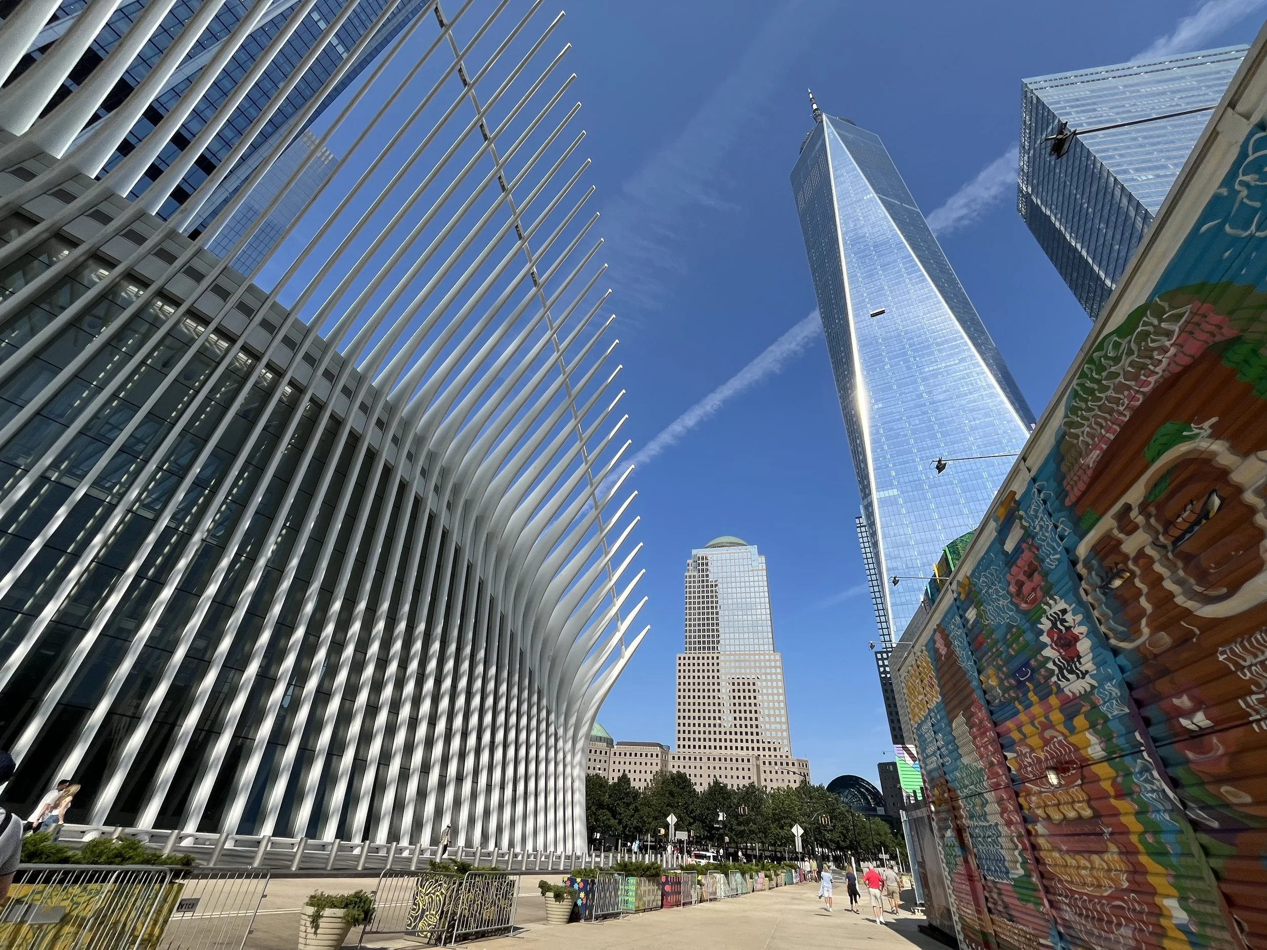Downtown New York City with modern skyscrapers, including One World Trade Center, against a clear blue sky.