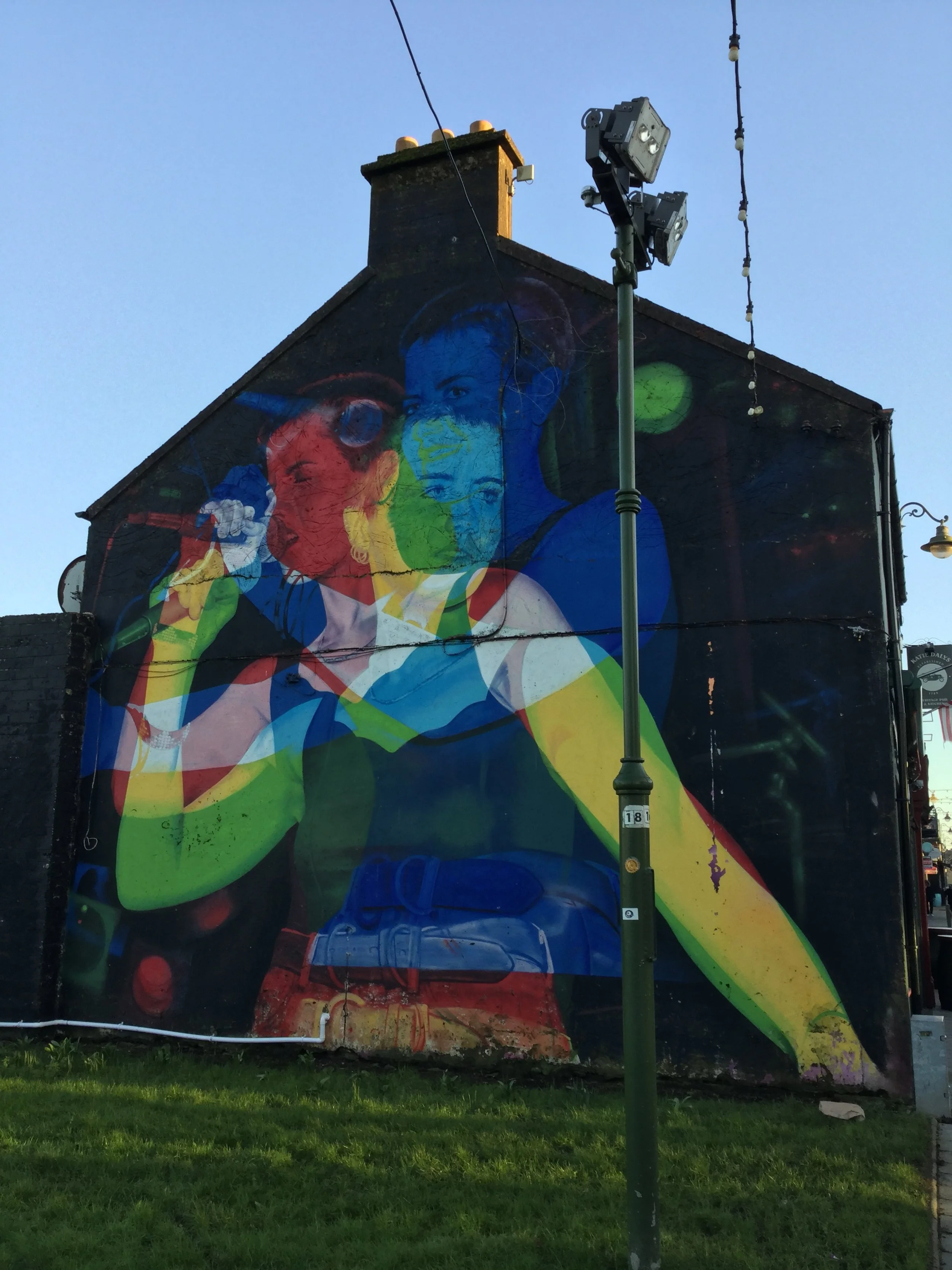 Colorful mural on a building wall depicting a woman holding a small dog, with multiple overlapping color layers creating an abstract, vibrant effect.