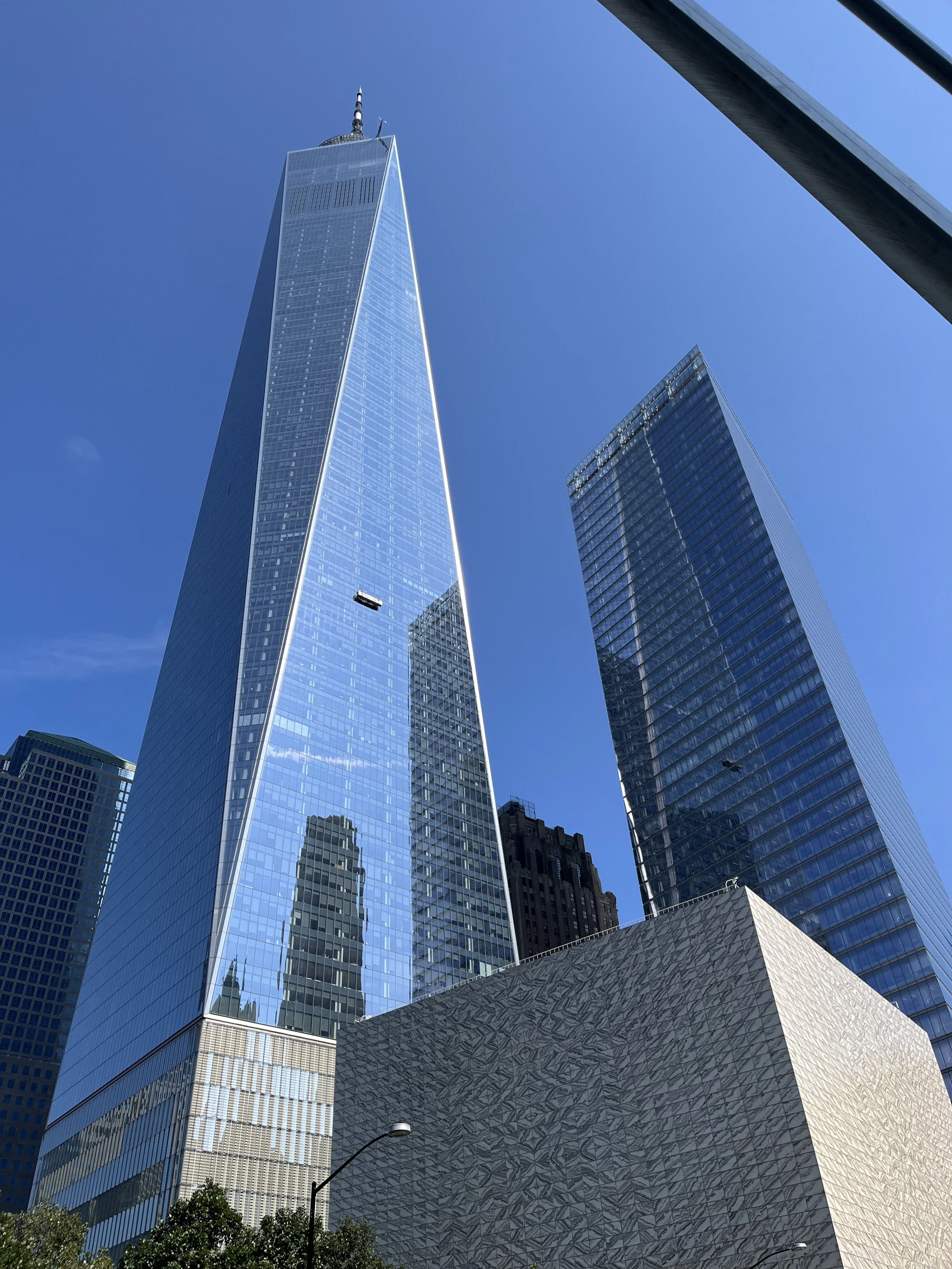 View of One World Trade Center and surrounding tall buildings in New York City under a clear blue sky.