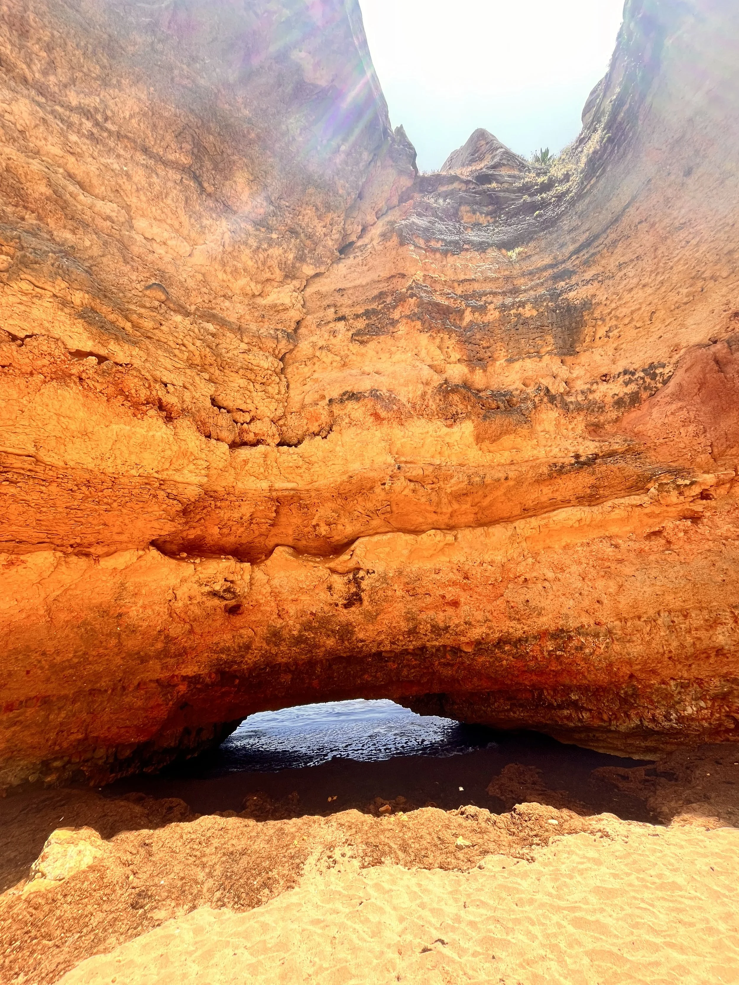 A natural rock formation with a large arch in the desert, with sand in the foreground and the ocean visible through the arch.