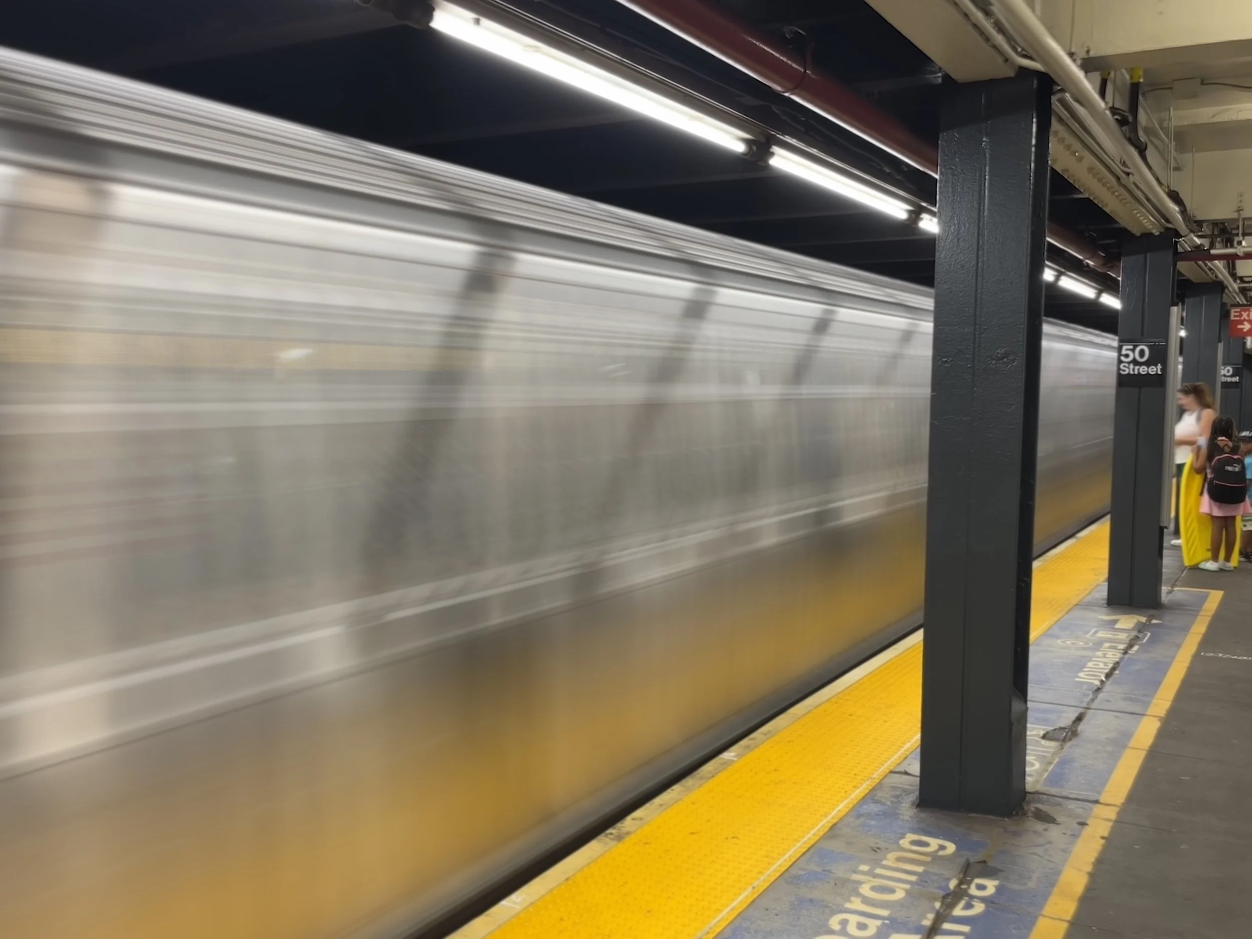 Subway train arriving at the station with blurred motion, platform with a yellow safety line, and a woman with a backpack waiting at the platform.