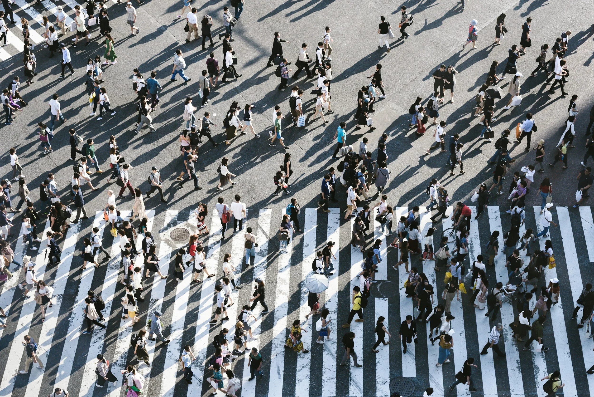 Aerial view of a crowded crosswalk with numerous pedestrians walking in various directions on a city street.