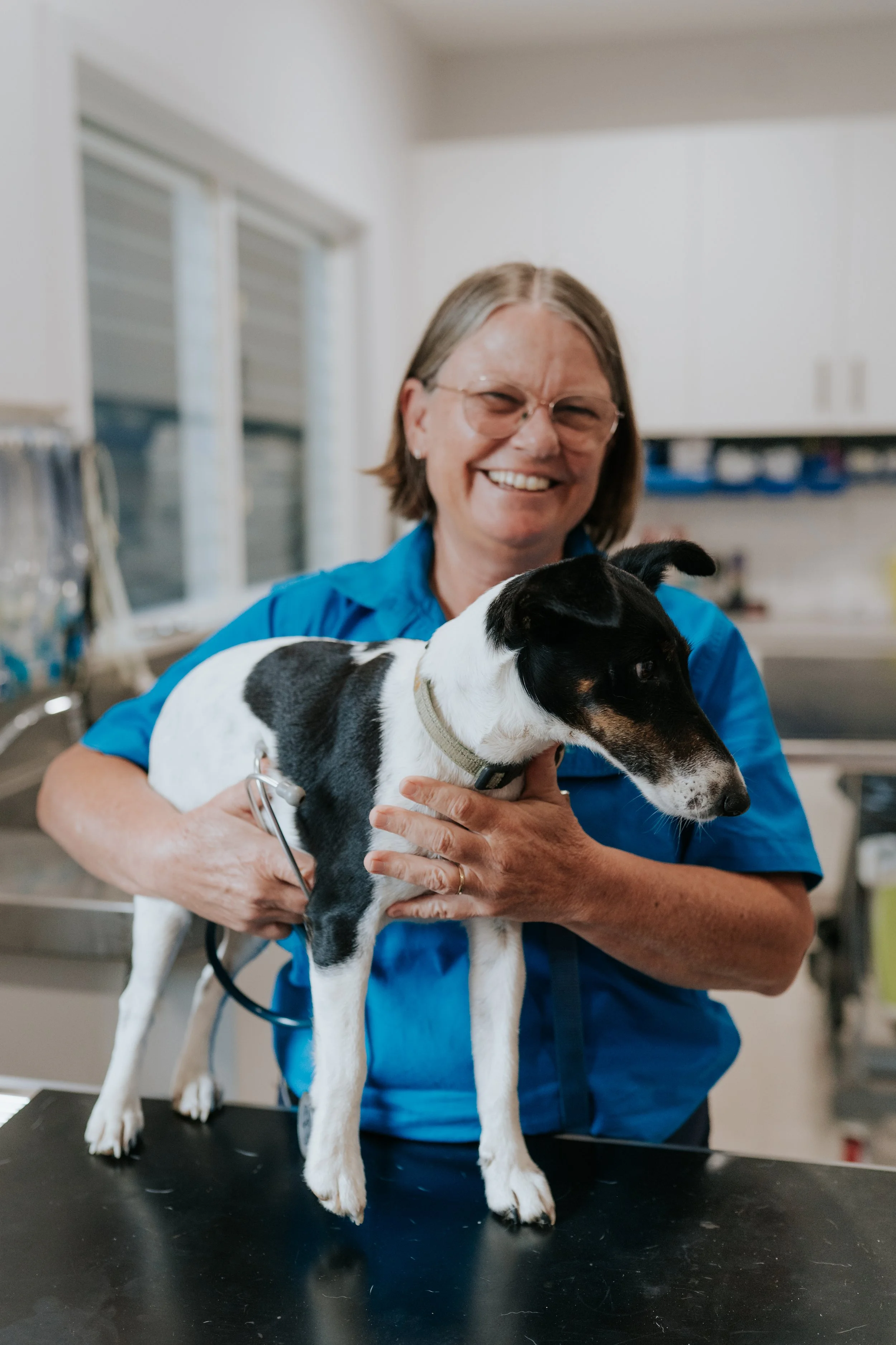 One of the friendly vets at Woolgoolga Vet Clinic is holding a small black and white dog and smiling.