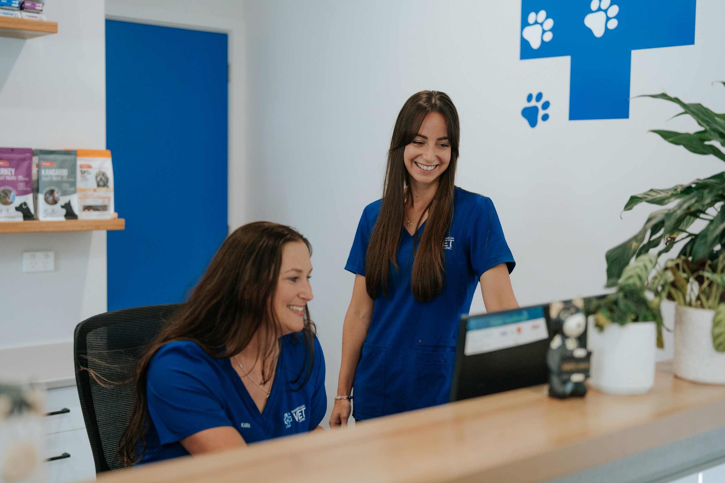 Two female staff man the desk at Woolgoolga Vet Clinic, with friendly smiles.