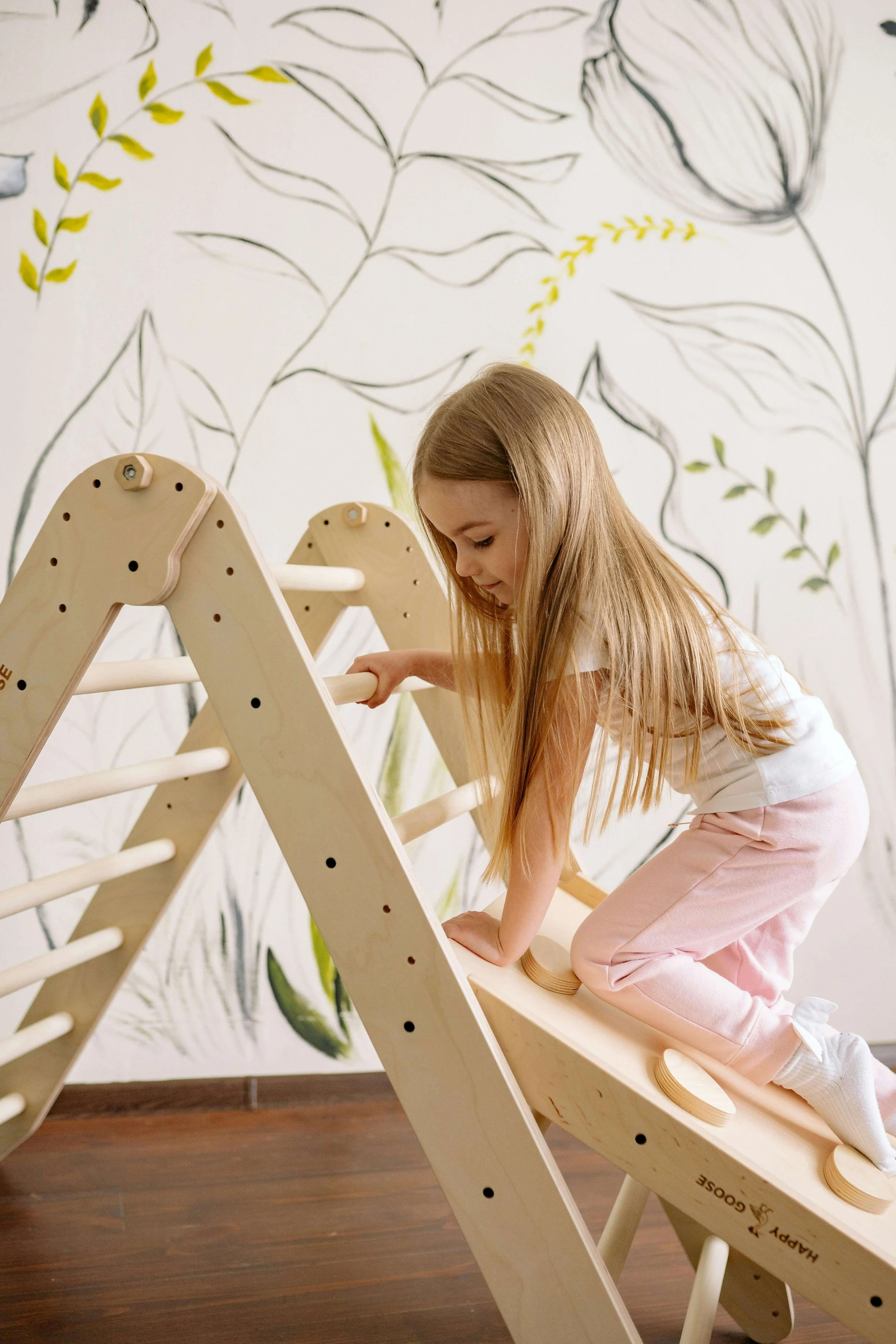 Young girl climbing up a pikler triangle