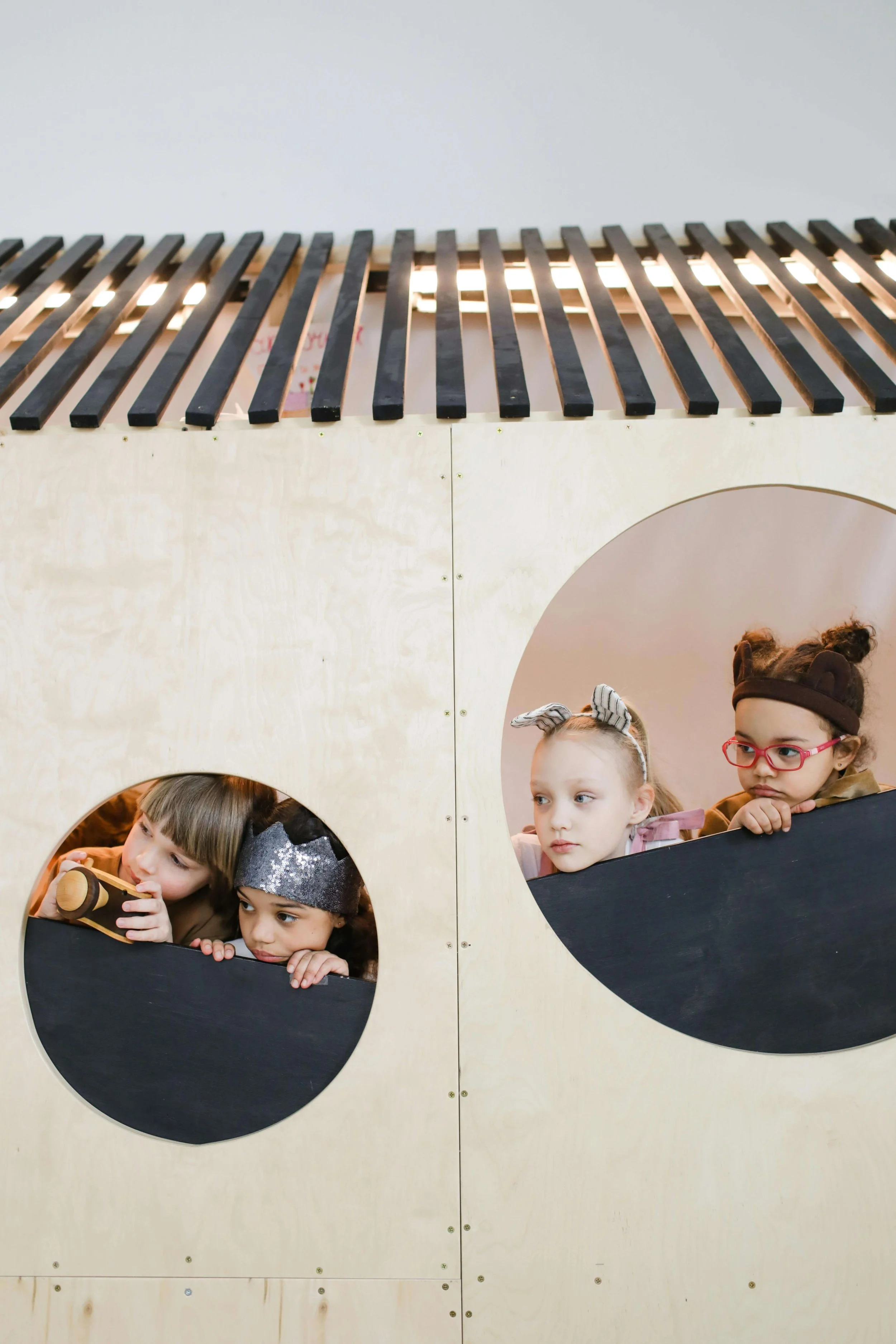 Children looking out of circle windows on a wooden play set