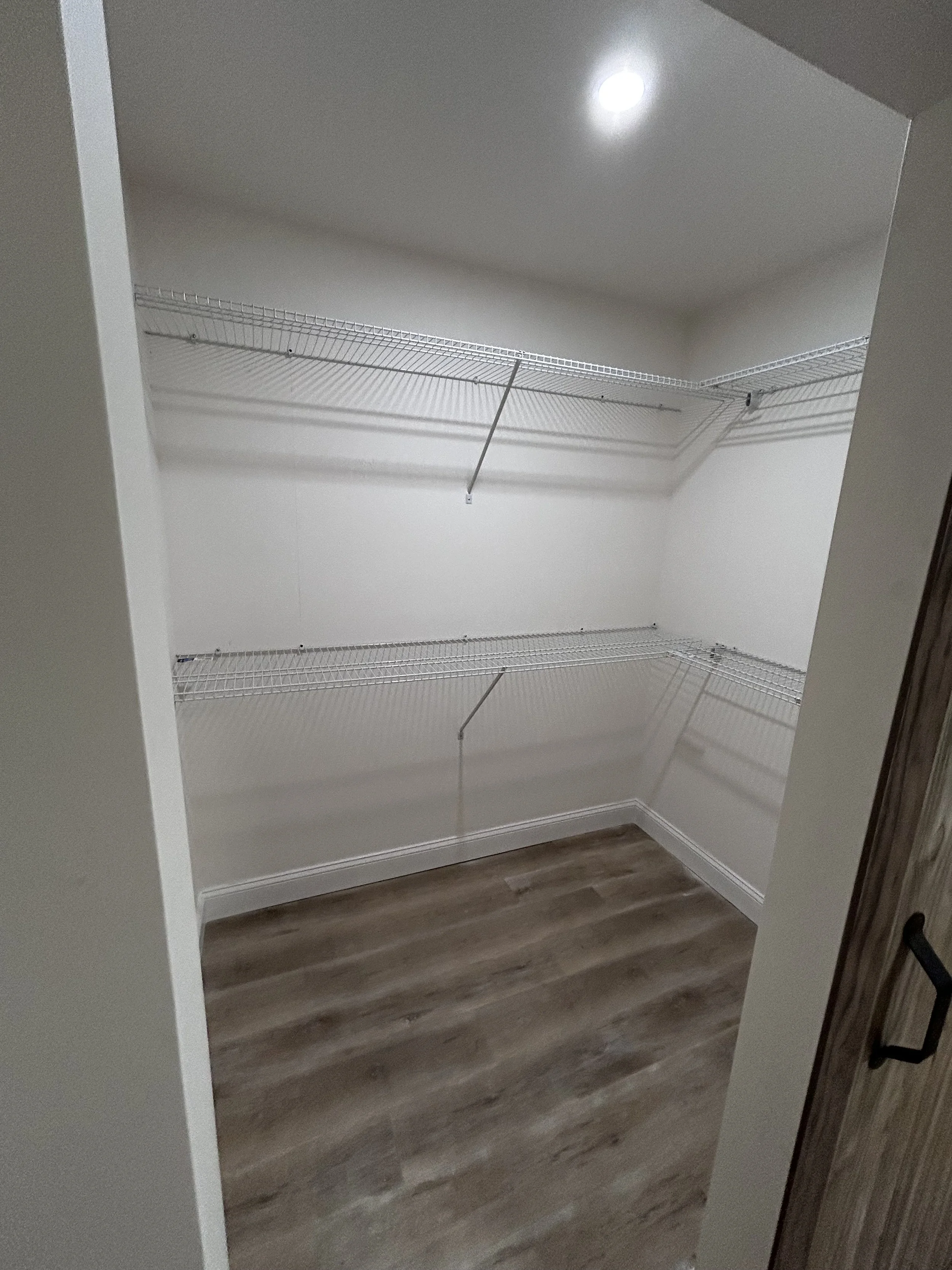 Empty walk-in closet with white wire shelving and wood-like vinyl flooring.