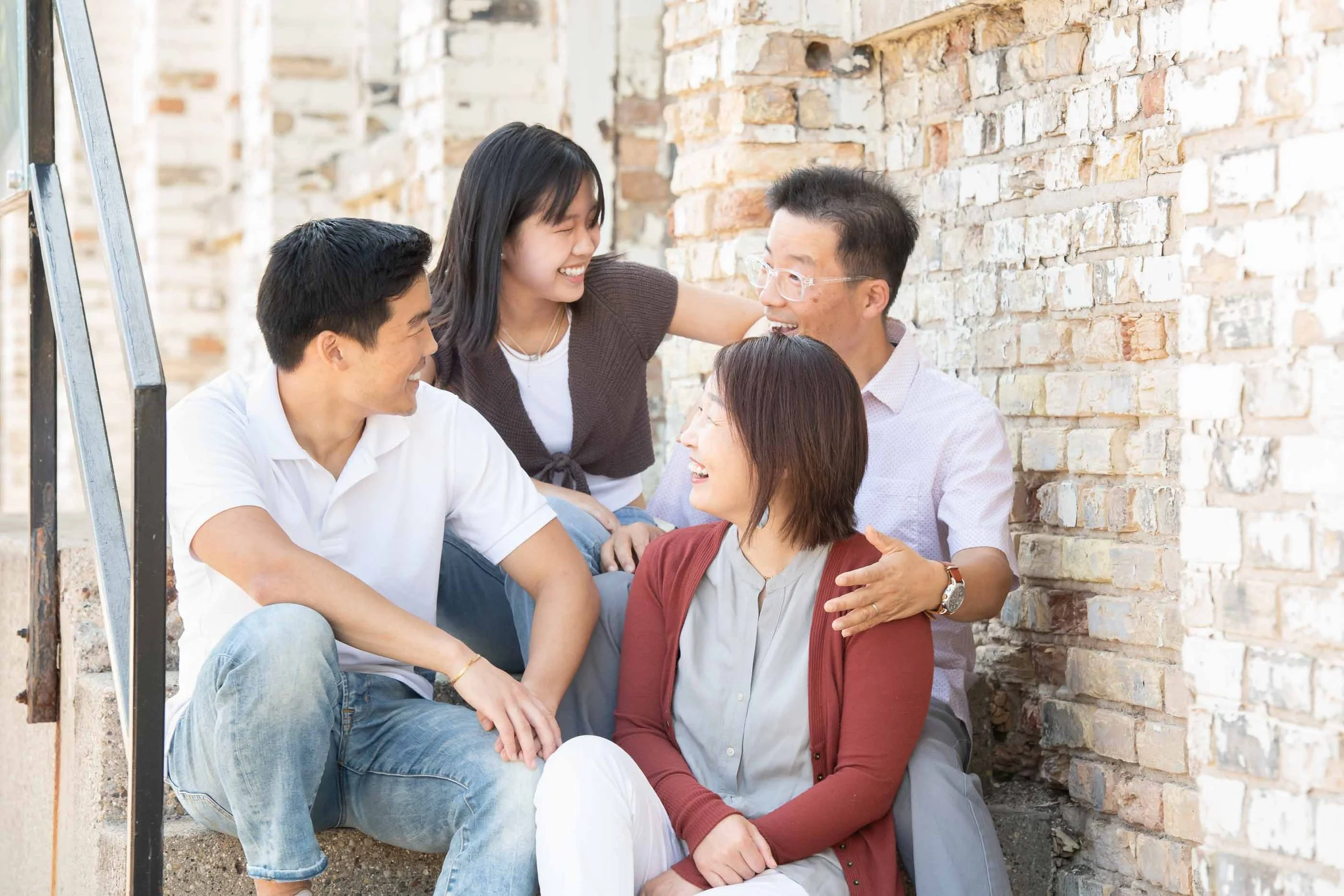 Group of five diverse people sitting on steps near a brick wall, smiling, and enjoying each other's company.