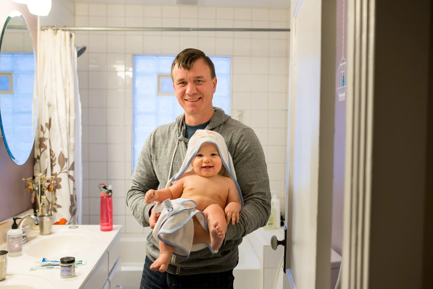 A man holding a smiling baby in a bathroom.