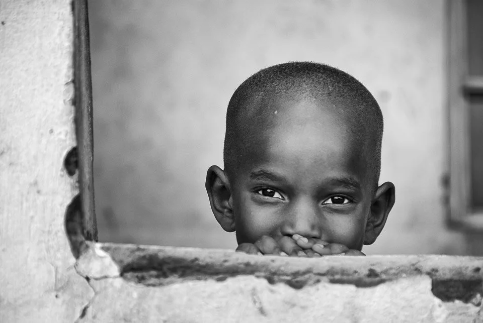 A young boy with a shaved head looking through a hole in a wall