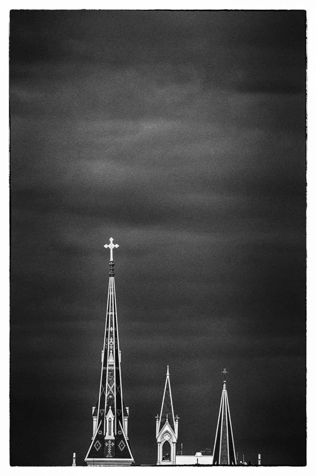 Black and white photograph of church steeples with crosses against a dark, cloudy sky.