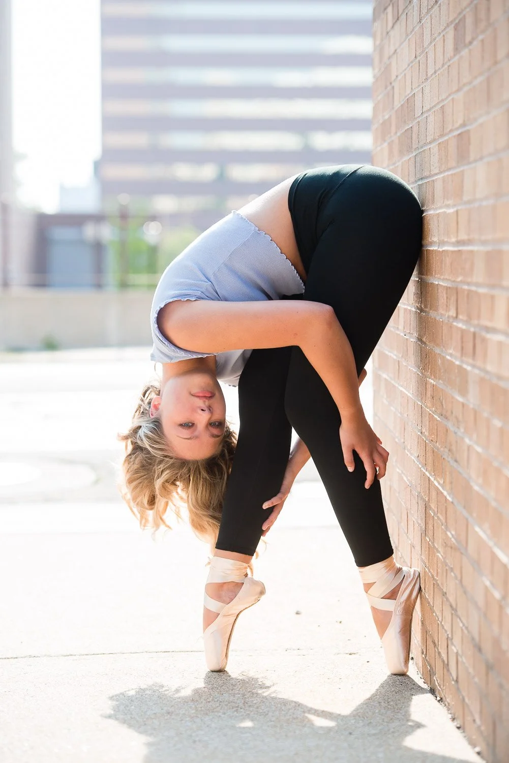 A woman in ballet attire practicing dance near a brick wall in an outdoor urban setting.