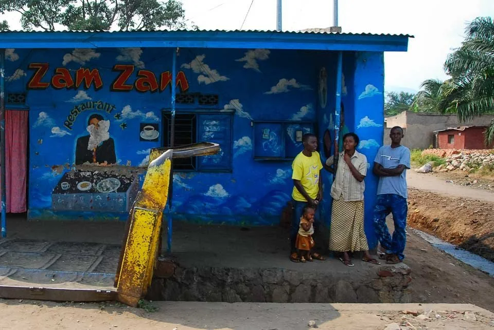 Four people and a child standing outside a small blue building with the sign 