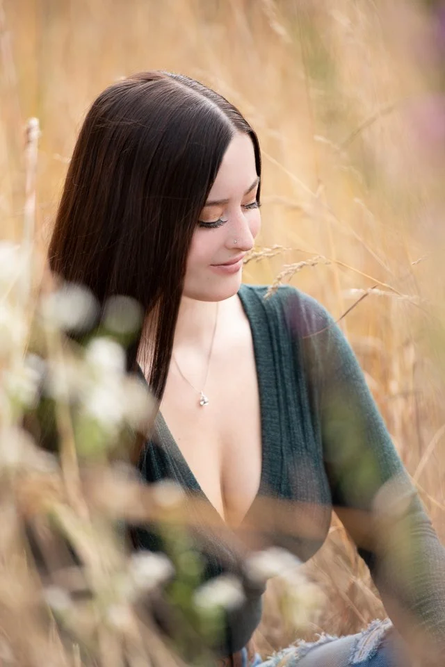 A woman with long dark hair and a nose piercing smiling softly in a field of tall, golden grass.