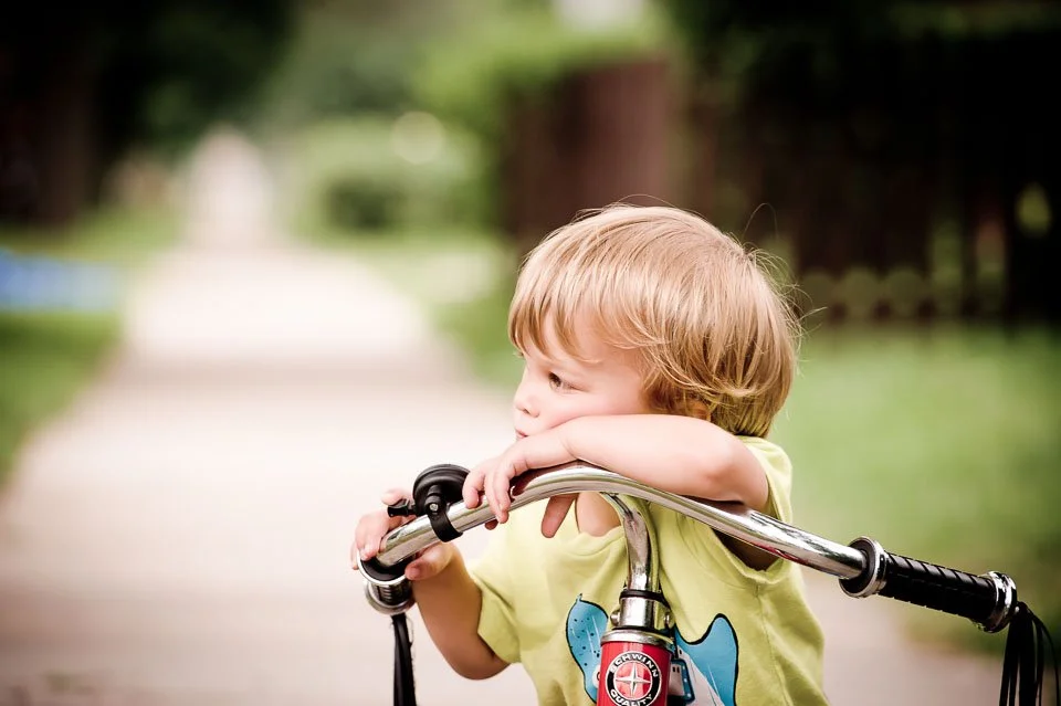 Young child resting on a bicycle handlebar outdoors on a park path