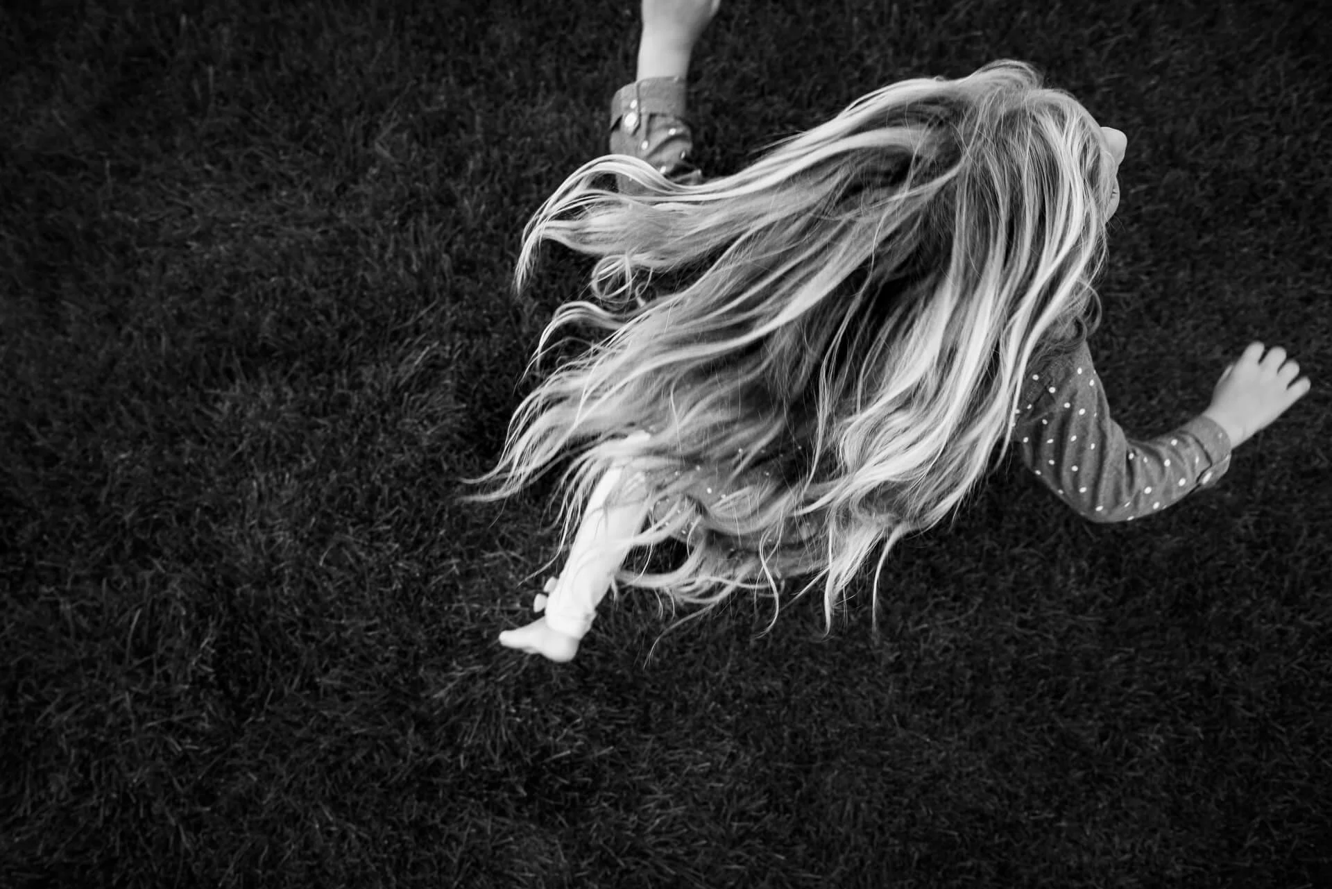 Child with long, wavy hair lying on grass, viewed from above.