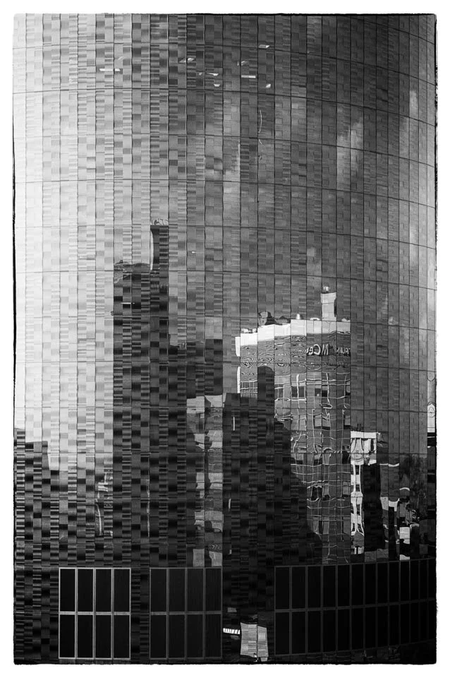 Reflective glass building with distorted cityscape reflections in black and white.