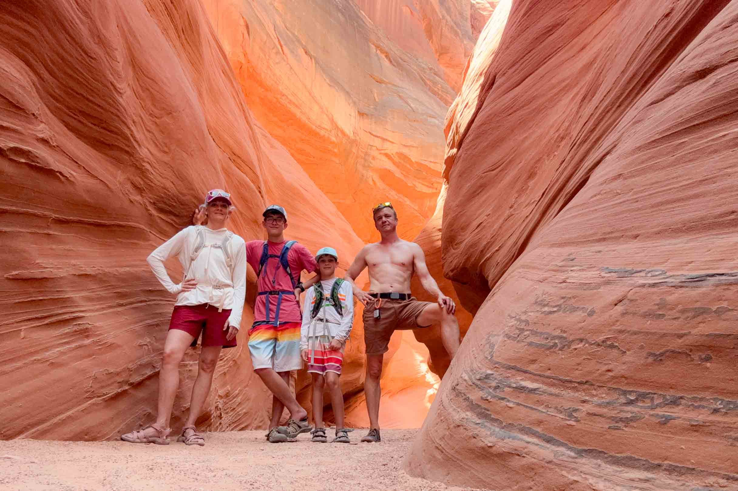 Family of four posing inside a narrow, winding slot canyon with smooth, reddish-orange rock walls.