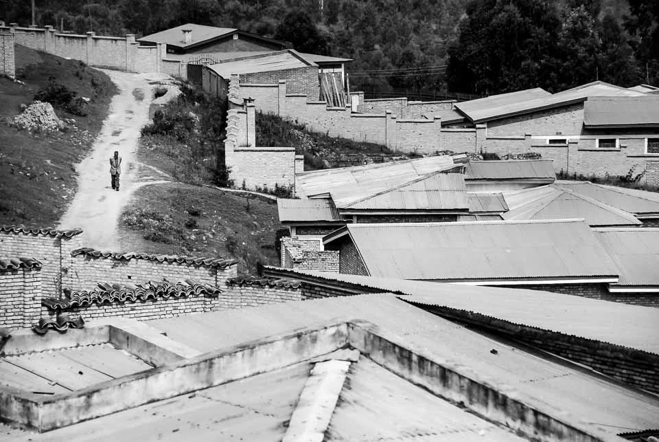 Black and white photo of a hilly neighborhood with houses, a dirt path, and one person walking on the path.