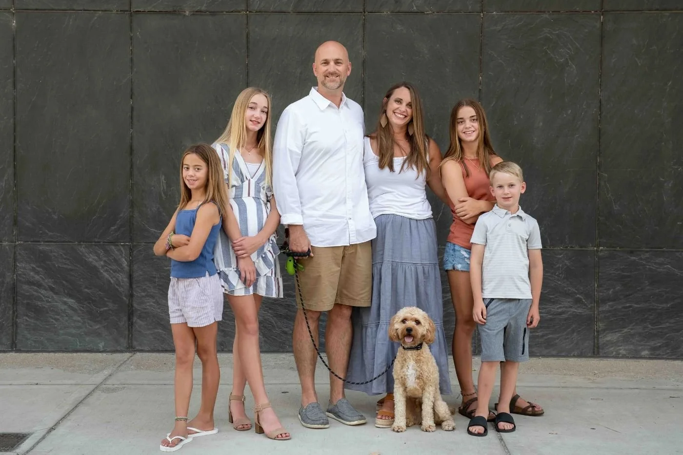 Byrne family of six with their dog posing together in matching neutral tones against a dark textured wall