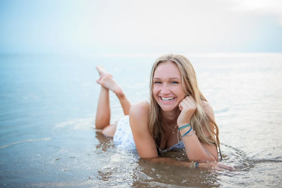 Young woman lying on her stomach in the water at the beach, smiling and looking at the camera.