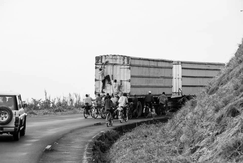 A group of people on bicycles trying to pass a large truck on a narrow road.
