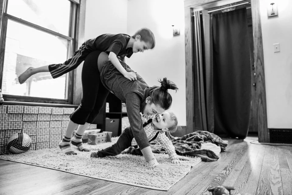A woman doing a handstand on a rug with two children on her back and in front of her in a living room.