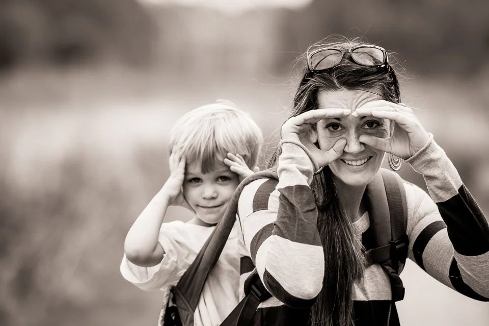 A woman and a young boy outdoors making playful binocular shapes with their hands.