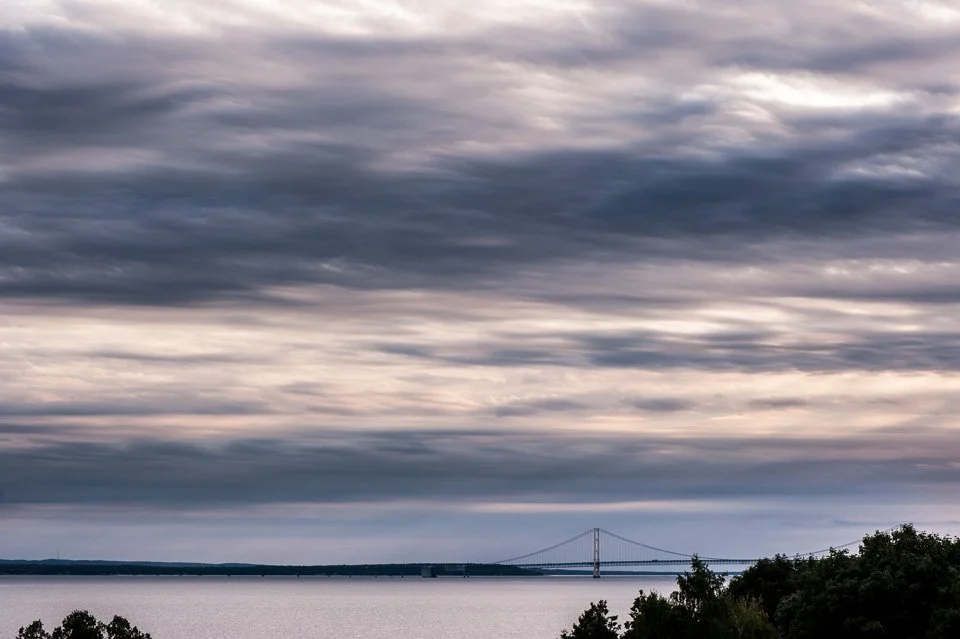 A bridge over a body of water under a cloudy sky with trees in the foreground.