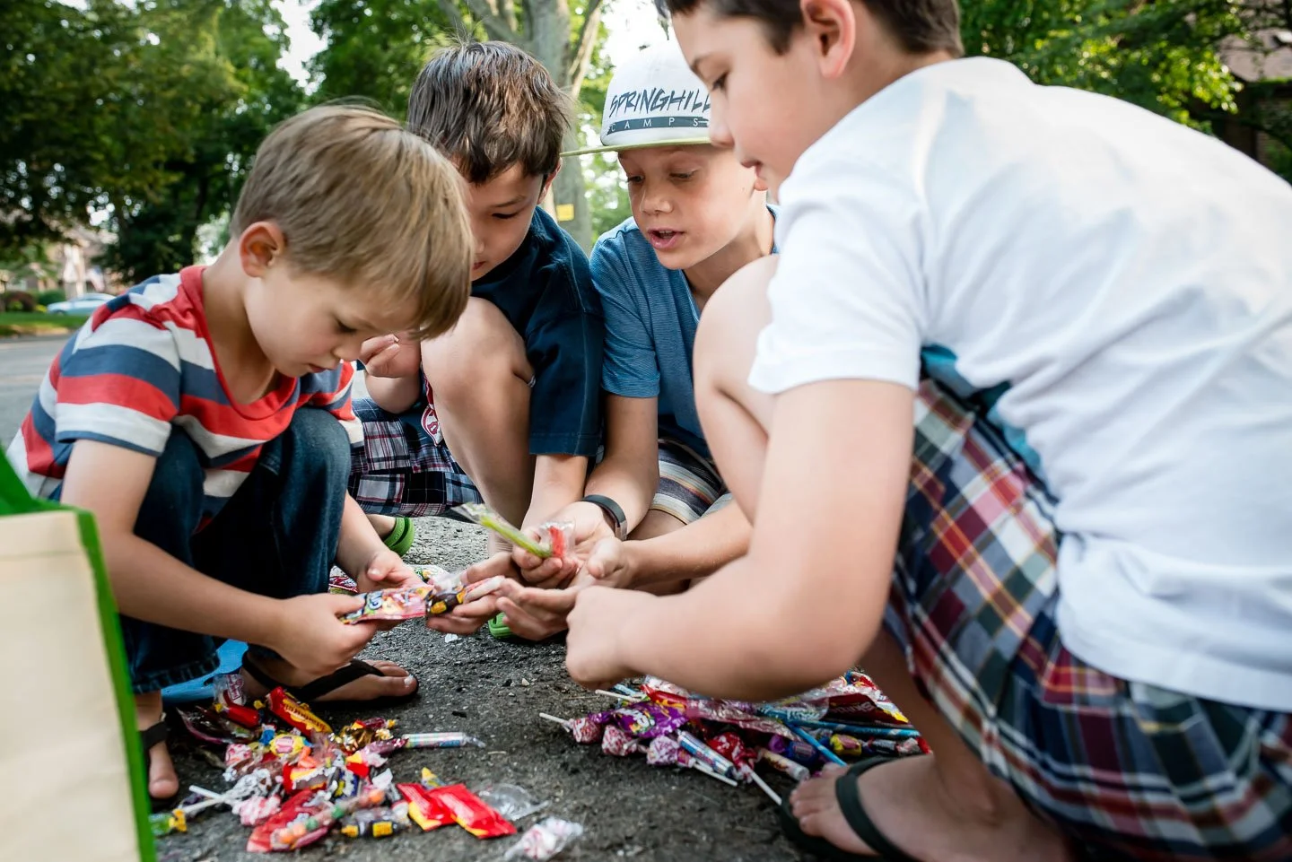 Group of children sitting on the ground outside, examining and playing with colorful candies and toys.