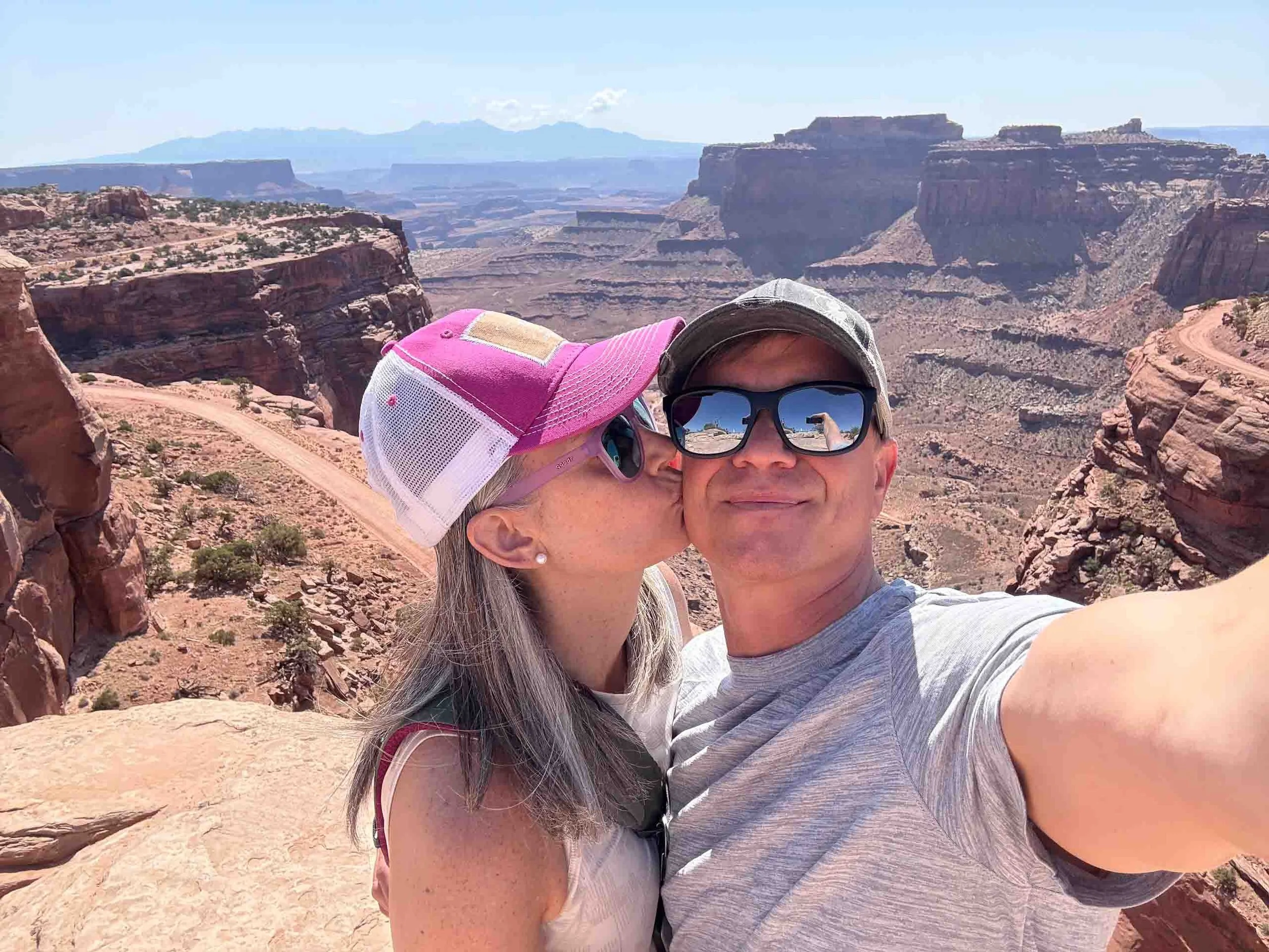 A couple takes a selfie at the Grand Canyon, with red rocks and canyon views in the background.