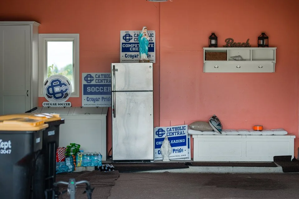 Indoor portion of a room with peach-colored walls and white furniture, including a refrigerator, a shelf with decorative items, a window, and sports-related posters and signs.