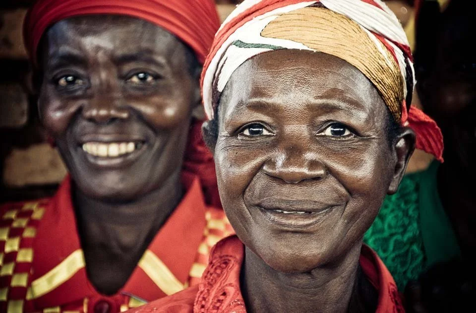 Two smiling women wearing traditional headscarves and colorful clothing.