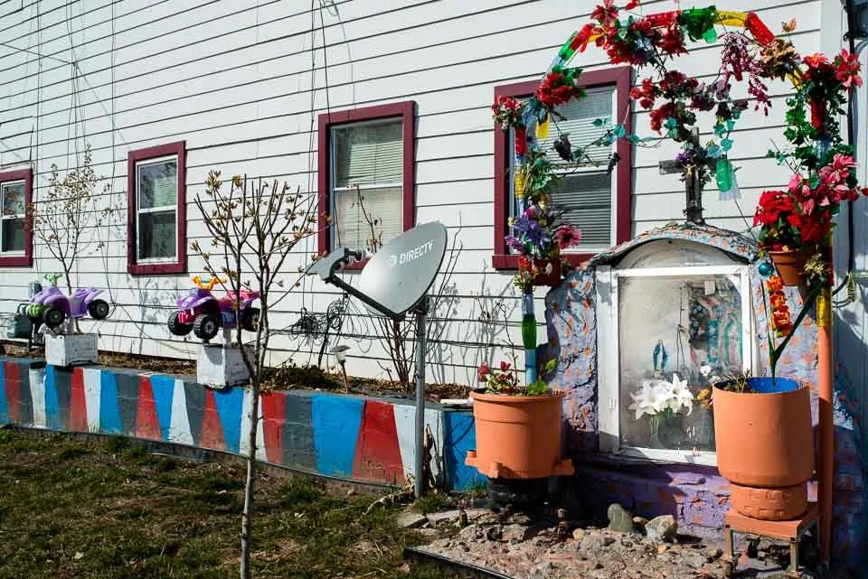 House exterior decorated with flowers, colorful painted curb, satellite dish, and toy cars.