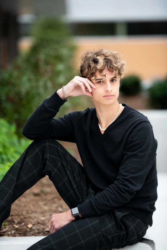Senior guy in modern black outfit sitting on urban steps during a Grand Rapids senior portrait session